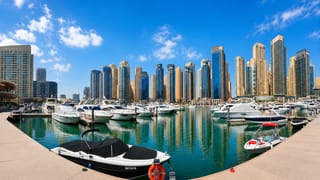 Dubai Marina's yacht-lined harbour backed by a dense cluster of waterfront skyscrapers under a clear blue sky.