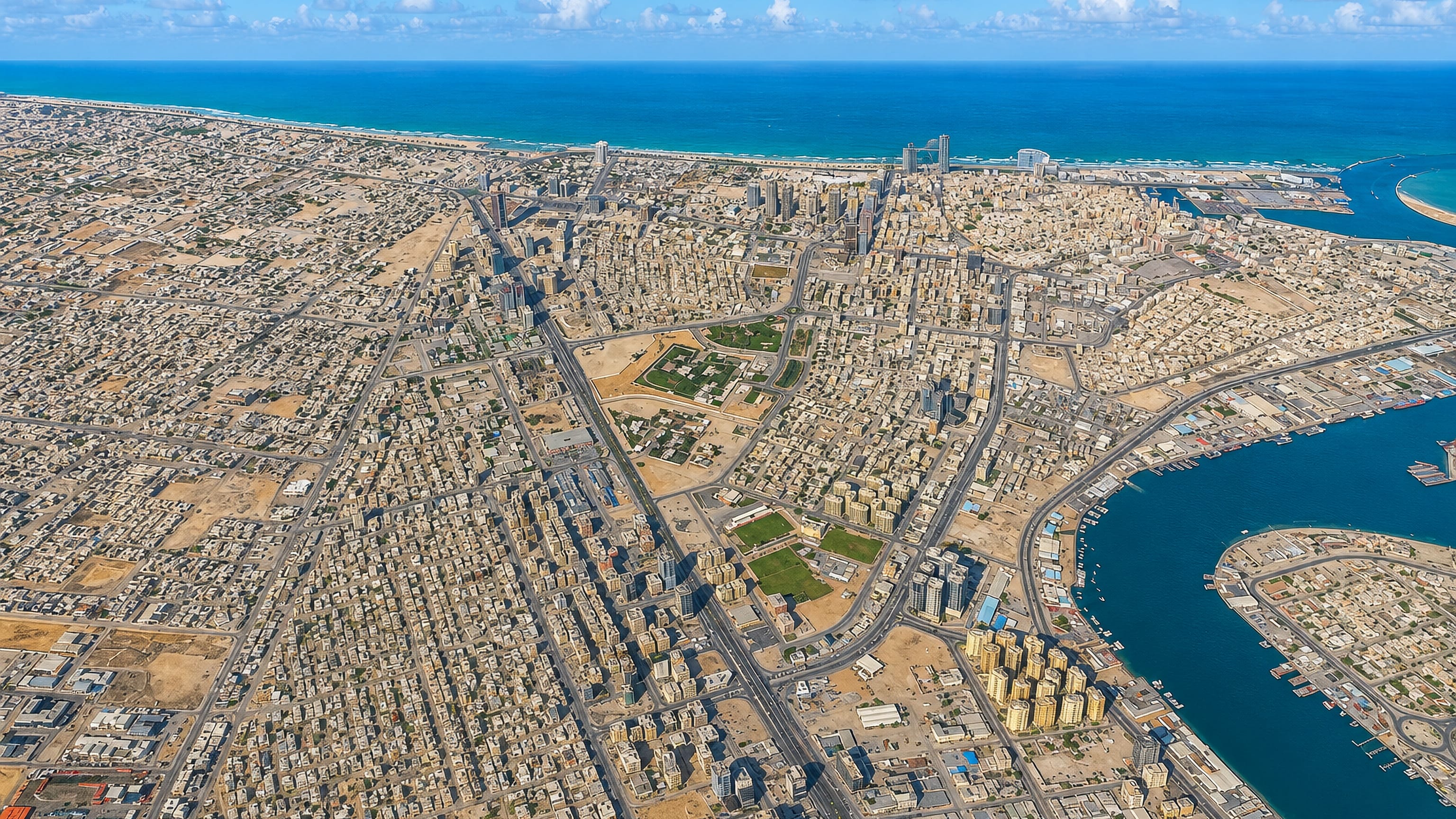 High aerial of Ajman spreading between its creek harbour and the Persian Gulf shoreline.