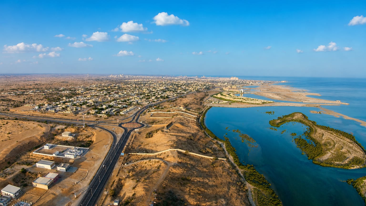 Aerial view of Ras Al Khaimah, a desert coastline with mangrove lagoons, a road interchange and a distant skyline.