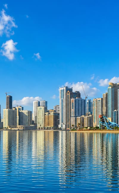 Sharjah's waterfront skyline of high-rise towers reflected in the calm blue water of Khalid Lagoon.