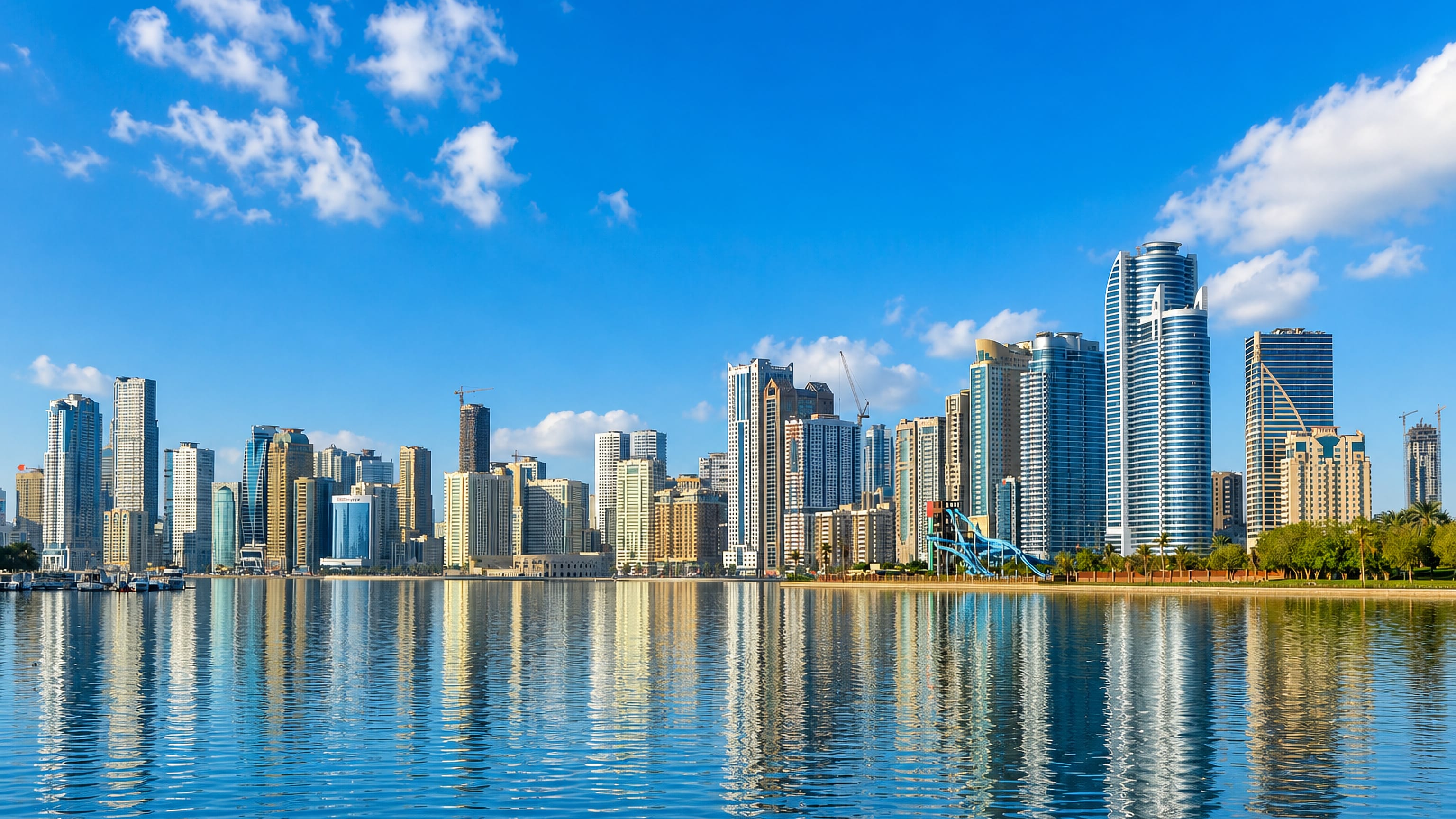 Sharjah's waterfront skyline of high-rise towers reflected in the calm blue water of Khalid Lagoon.