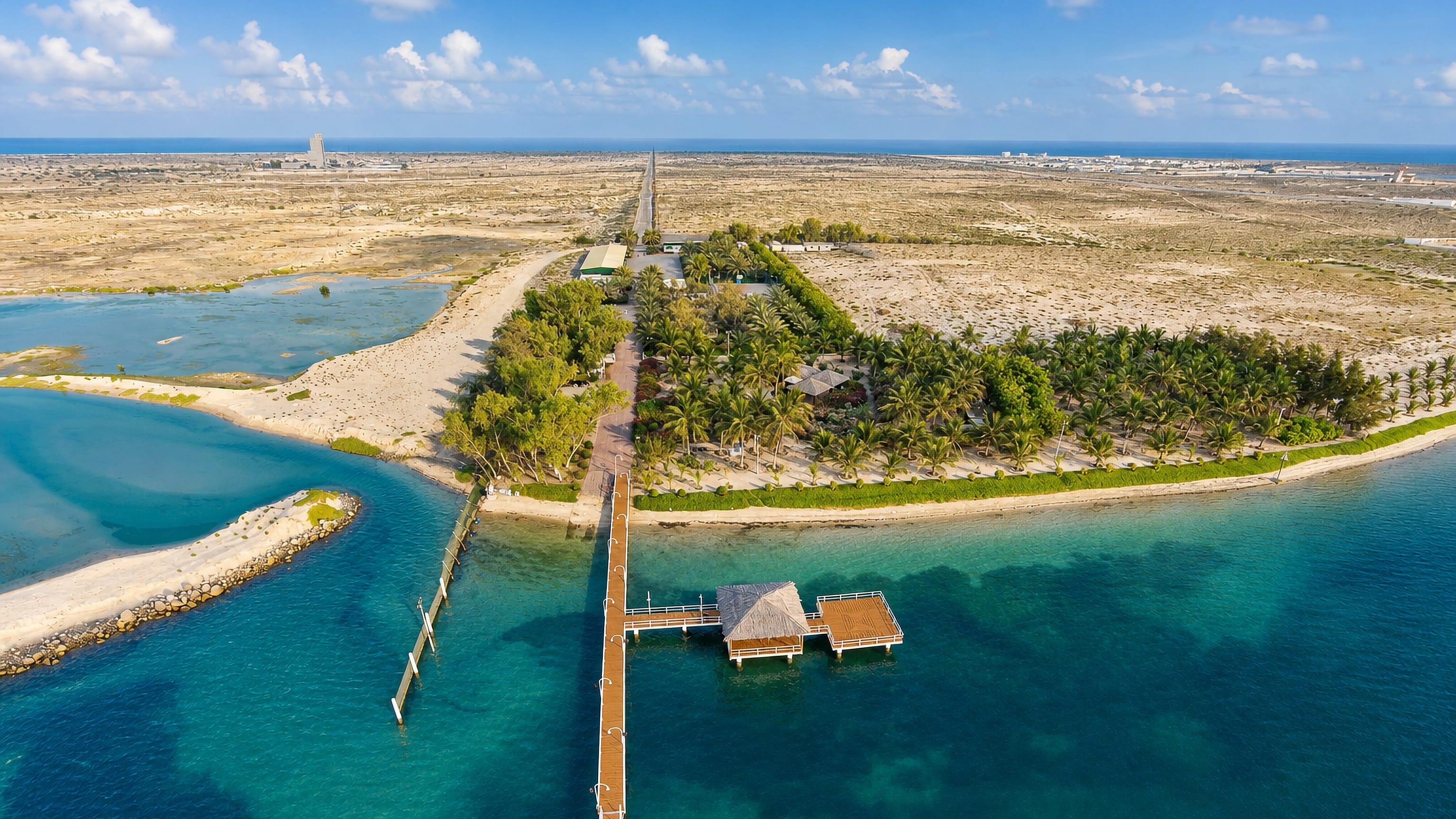 Wooden jetty reaching into the turquoise lagoon beside the palm-covered peninsula at Umm Al Quwain, UAE.