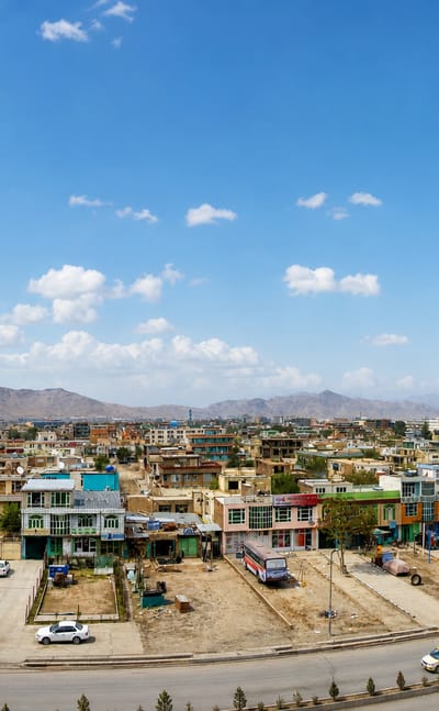 Low colorful buildings of Kabul sprawling toward arid mountains under a blue sky.