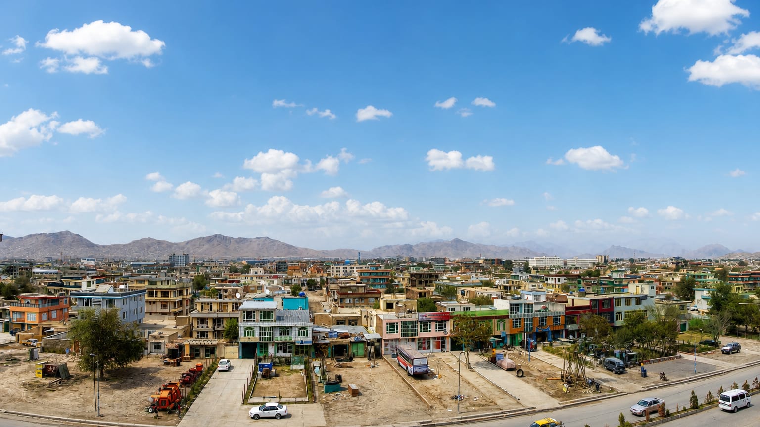 Low colorful buildings of Kabul sprawling toward arid mountains under a blue sky.