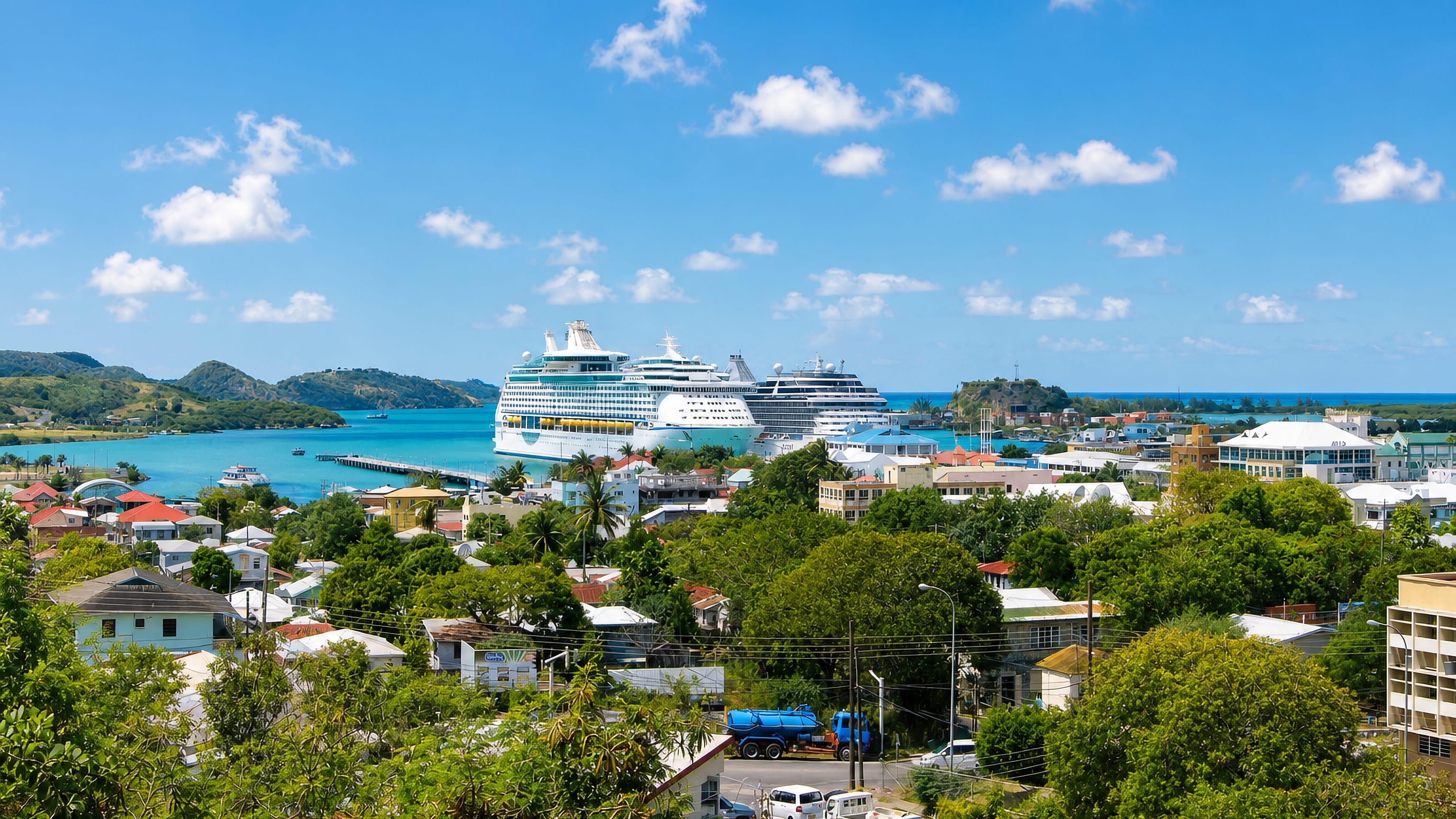Cruise ships berthed in Saint John's harbour, Antigua, seen over green hillside rooftops and turquoise water.
