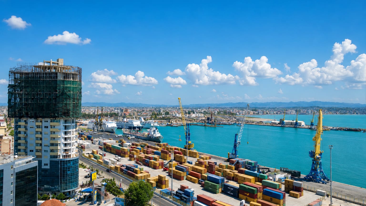 Durrës, Albania, container port with cranes and ferries beside a high-rise building under construction.