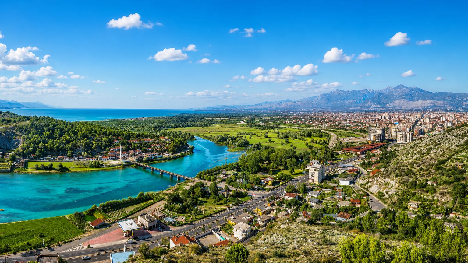 Shkodër, Albania, with the turquoise Buna River, a bridge and the Albanian Alps beyond the red-roofed city.