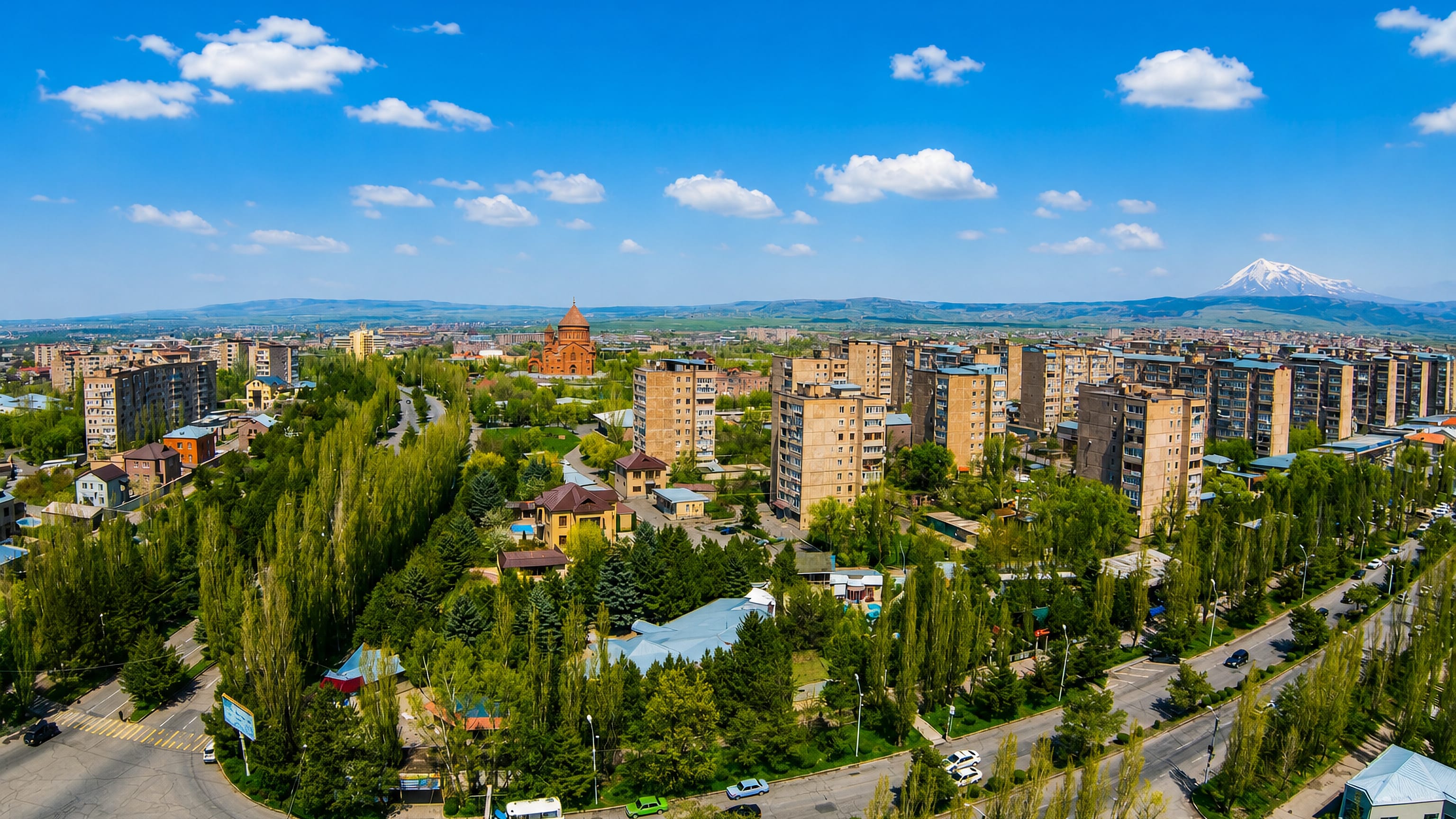 Aerial view of Abovyan, Armenia, its apartment blocks and red-stone church below snow-capped Mount Ararat.