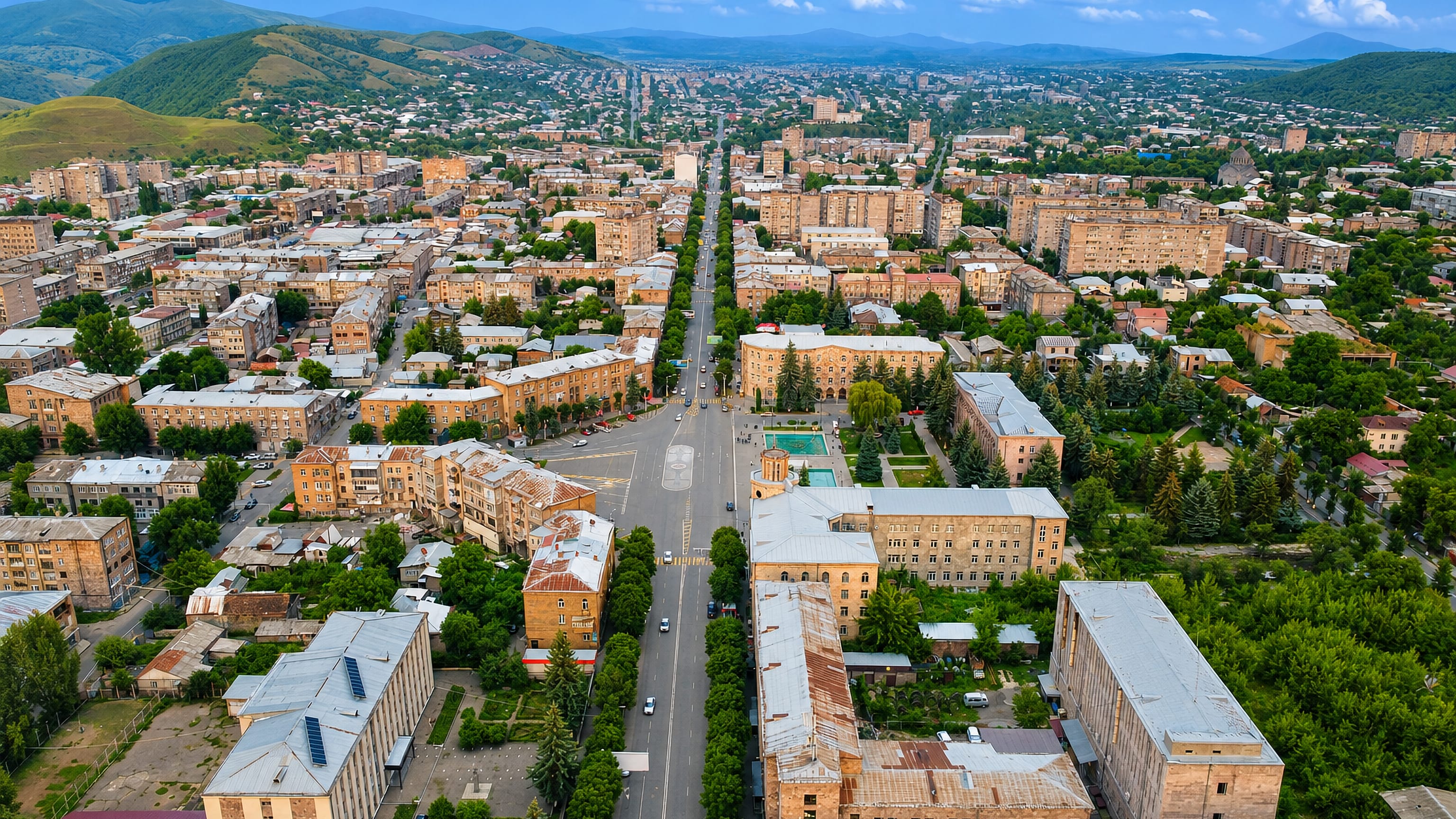 Aerial view along Vanadzor's main avenue and central square, ringed by the green Lori mountains.