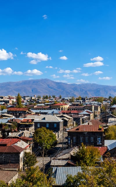 View over Gyumri's 19th-century stone rooftops and church spire with snow-capped mountains beyond.
