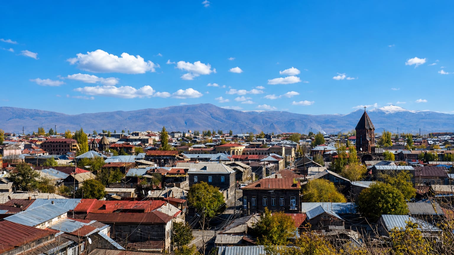 View over Gyumri's 19th-century stone rooftops and church spire with snow-capped mountains beyond.