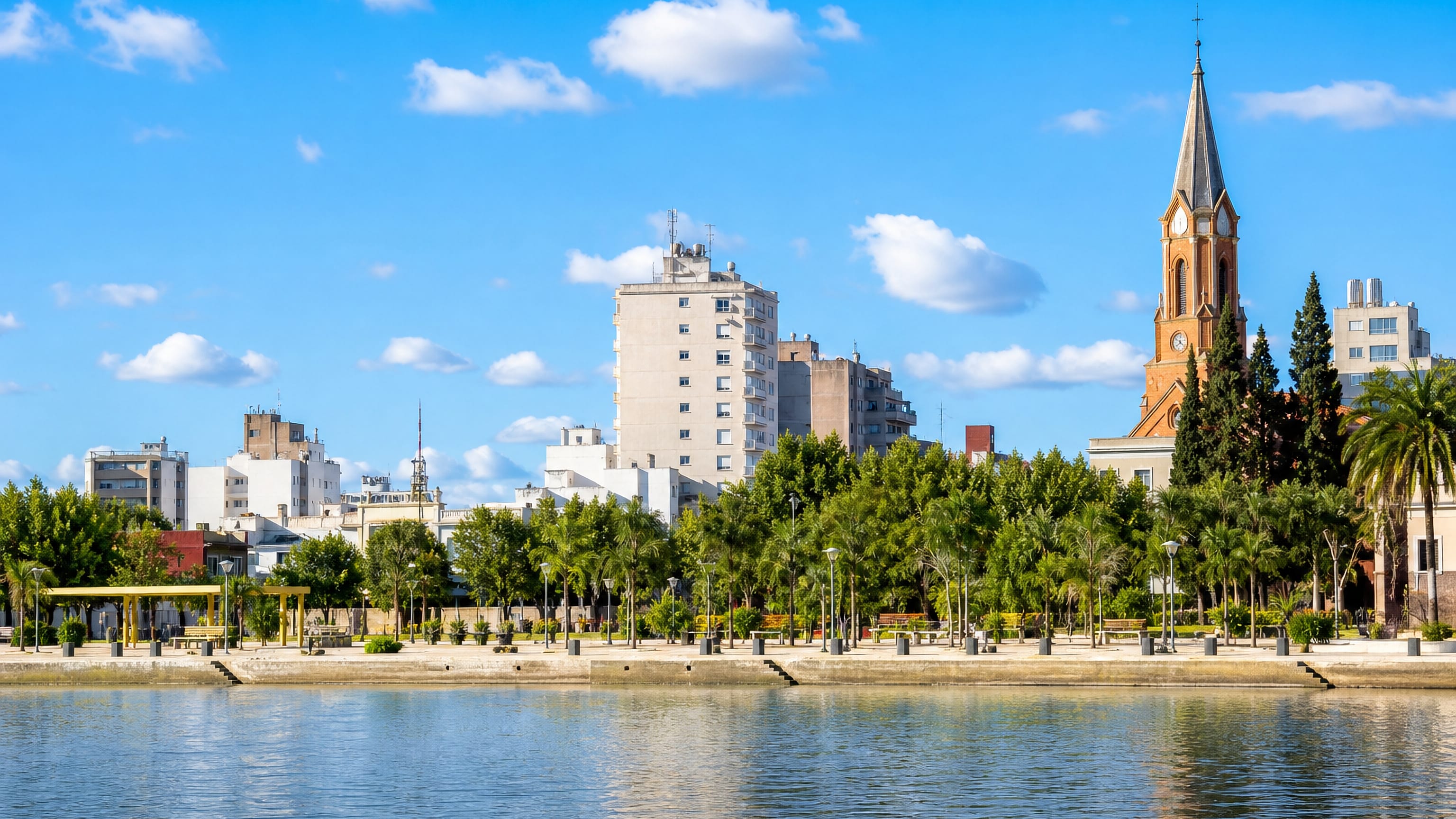 Villa Mercedes, Argentina, seen across the water, with a brick church tower rising above a palm-lined promenade.