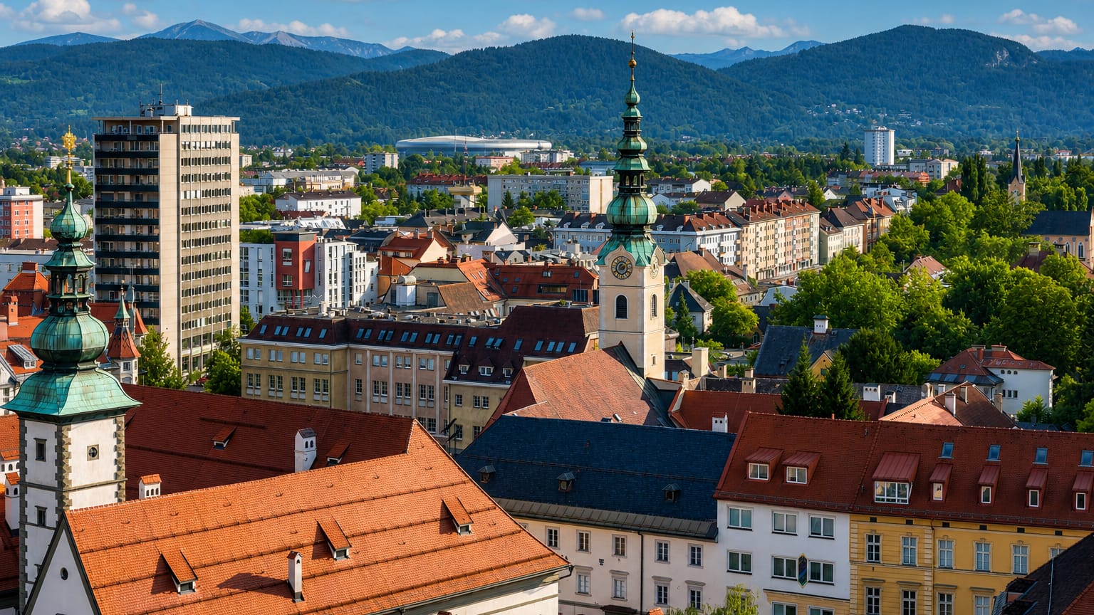 Baroque green-domed church towers and red-tiled rooftops of Klagenfurt am Worthersee with alpine peaks behind.