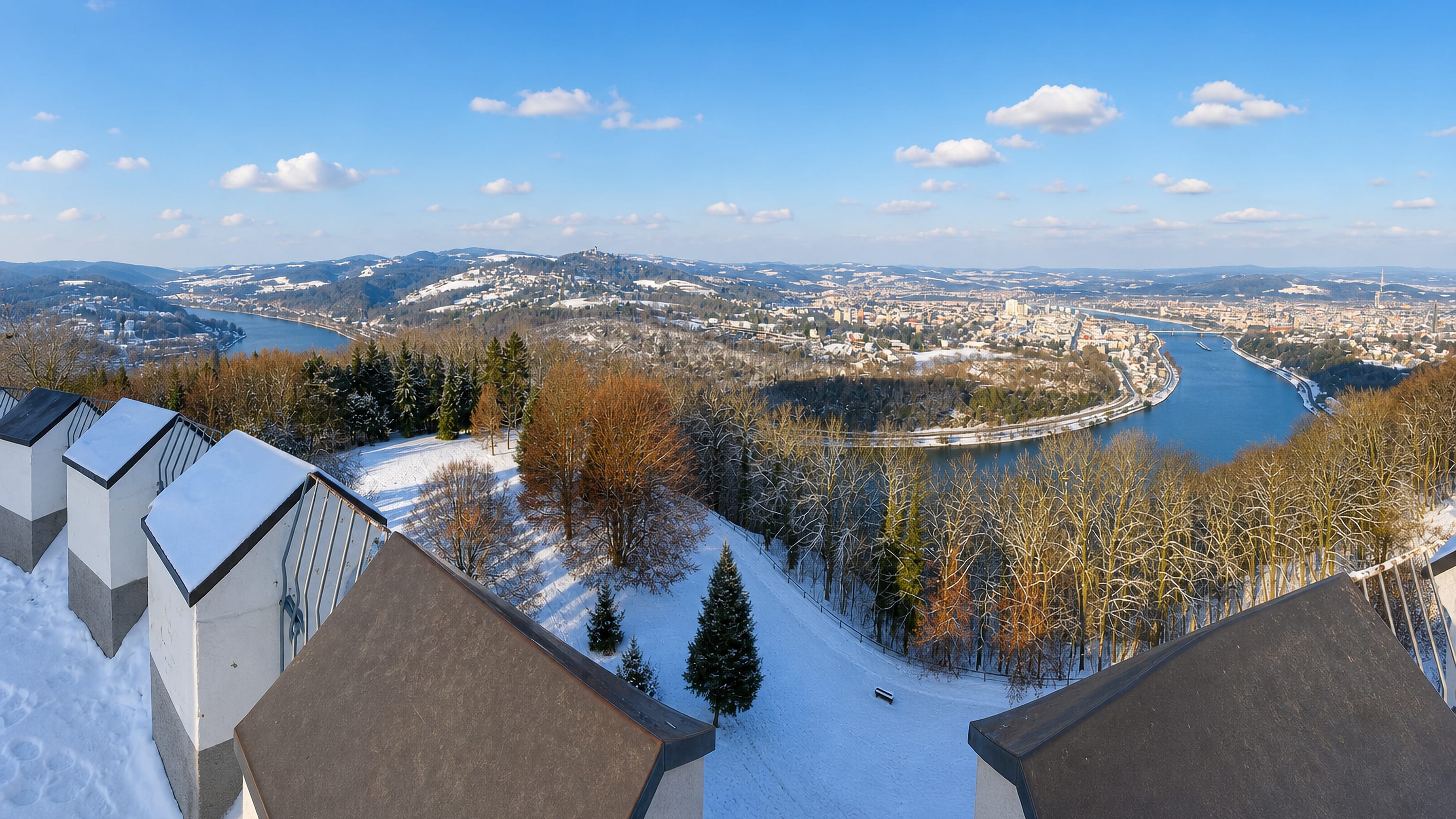 Winter view from Linz's Freinberg hill over the Danube bend and the city centre under a blue sky.