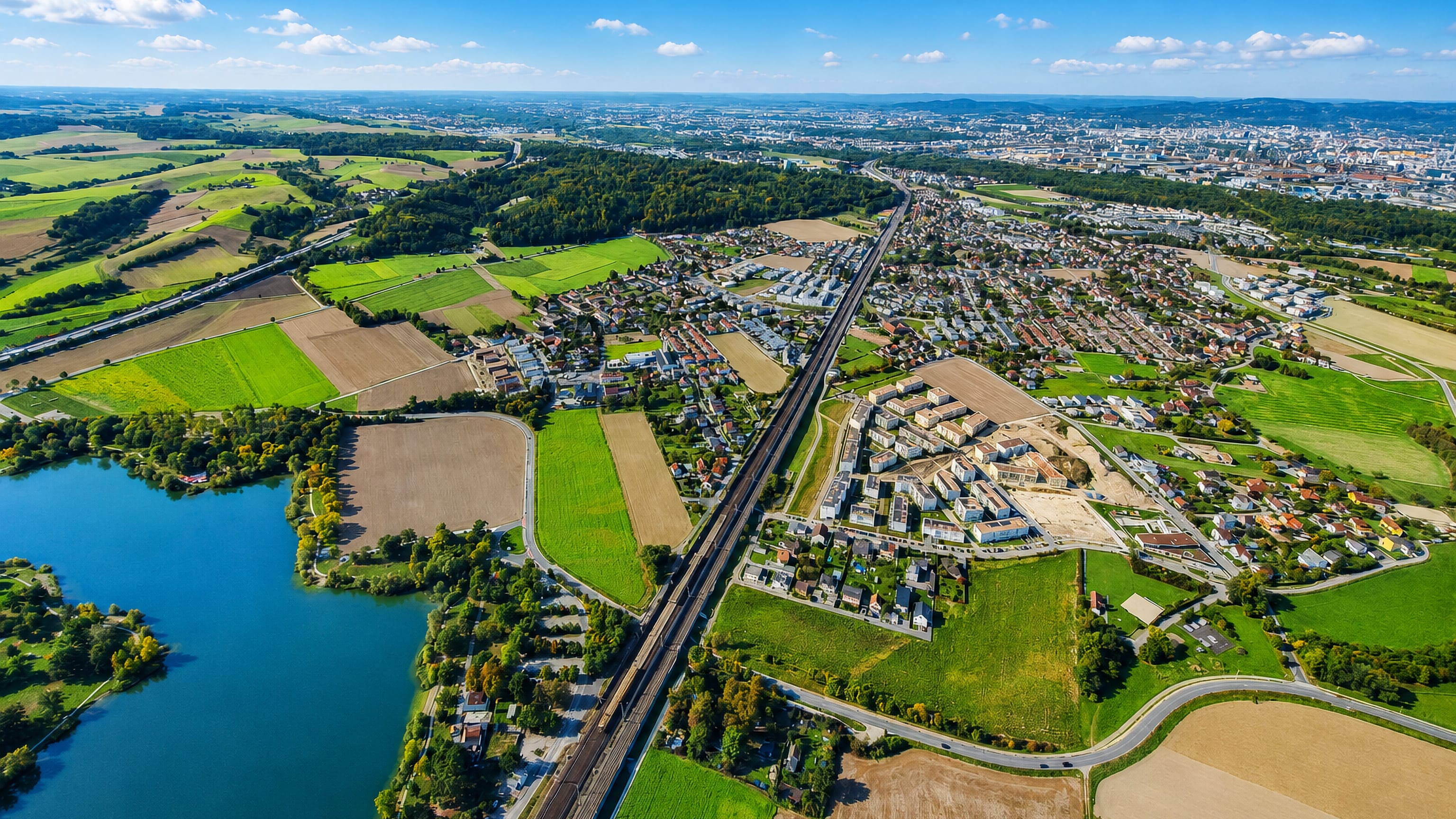 Aerial view of Pichling in Linz, with the Pichlinger See, the rail line and the city skyline beyond.