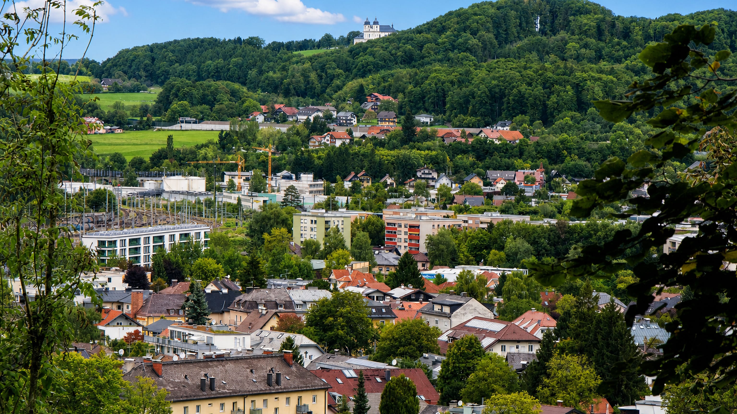 Gnigl in eastern Salzburg, with houses and rail yards in the valley below a wooded hill and hilltop church