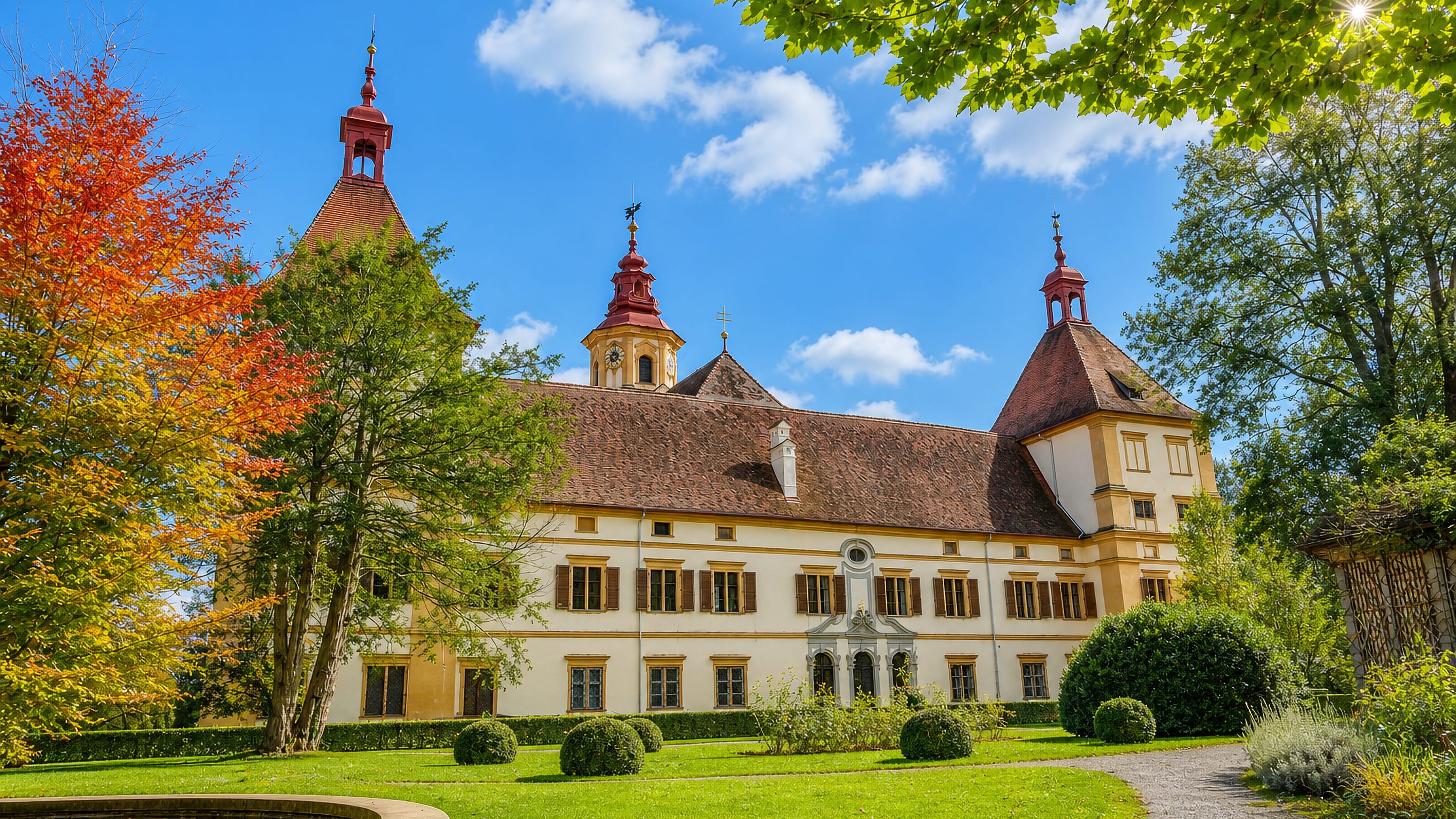 Schloss Eggenberg's cream Renaissance facade and red-roofed corner towers above its gardens in Graz.