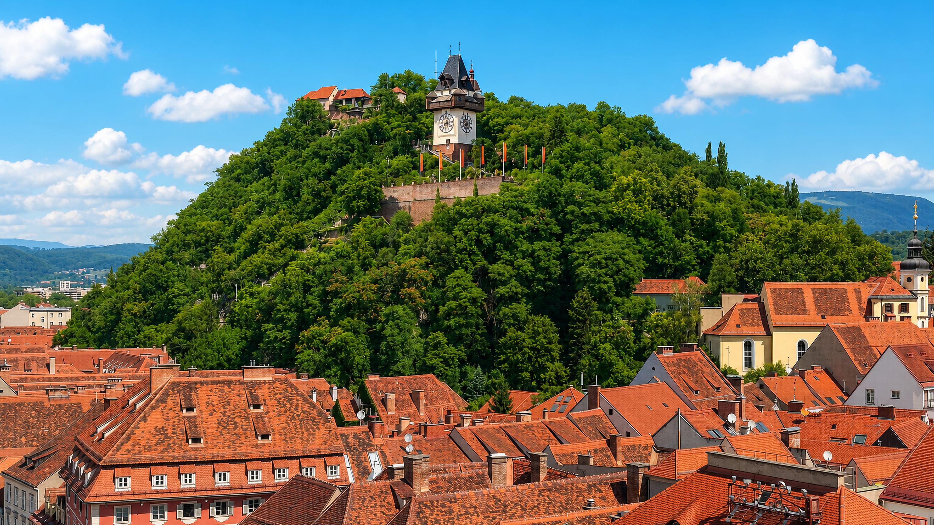 The Schlossberg clock tower above the red-tiled roofs of the Innere Stadt, Graz's old town core.