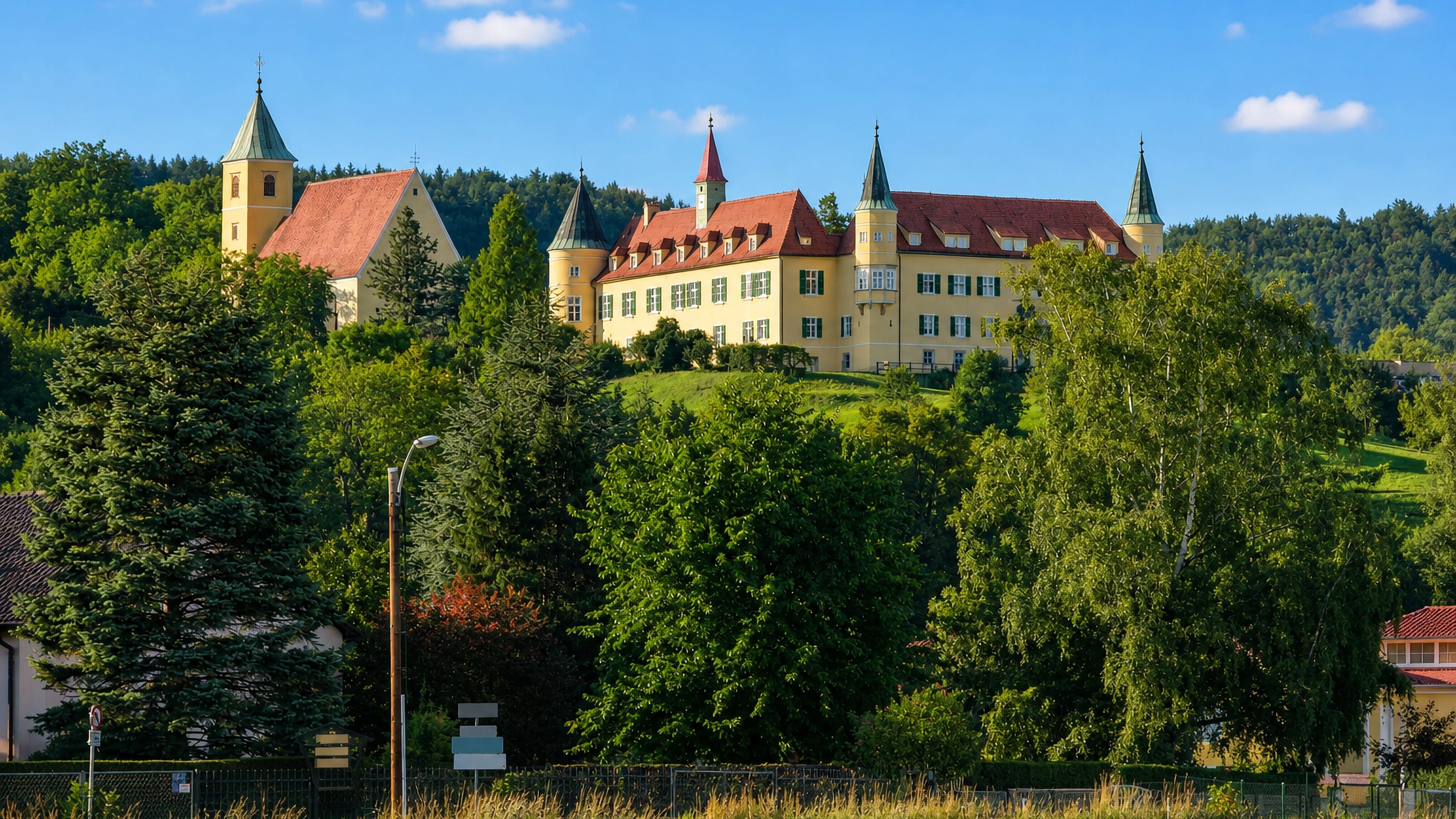 Schloss St. Martin's yellow turrets and a church tower above wooded slopes in Strassgang, Graz