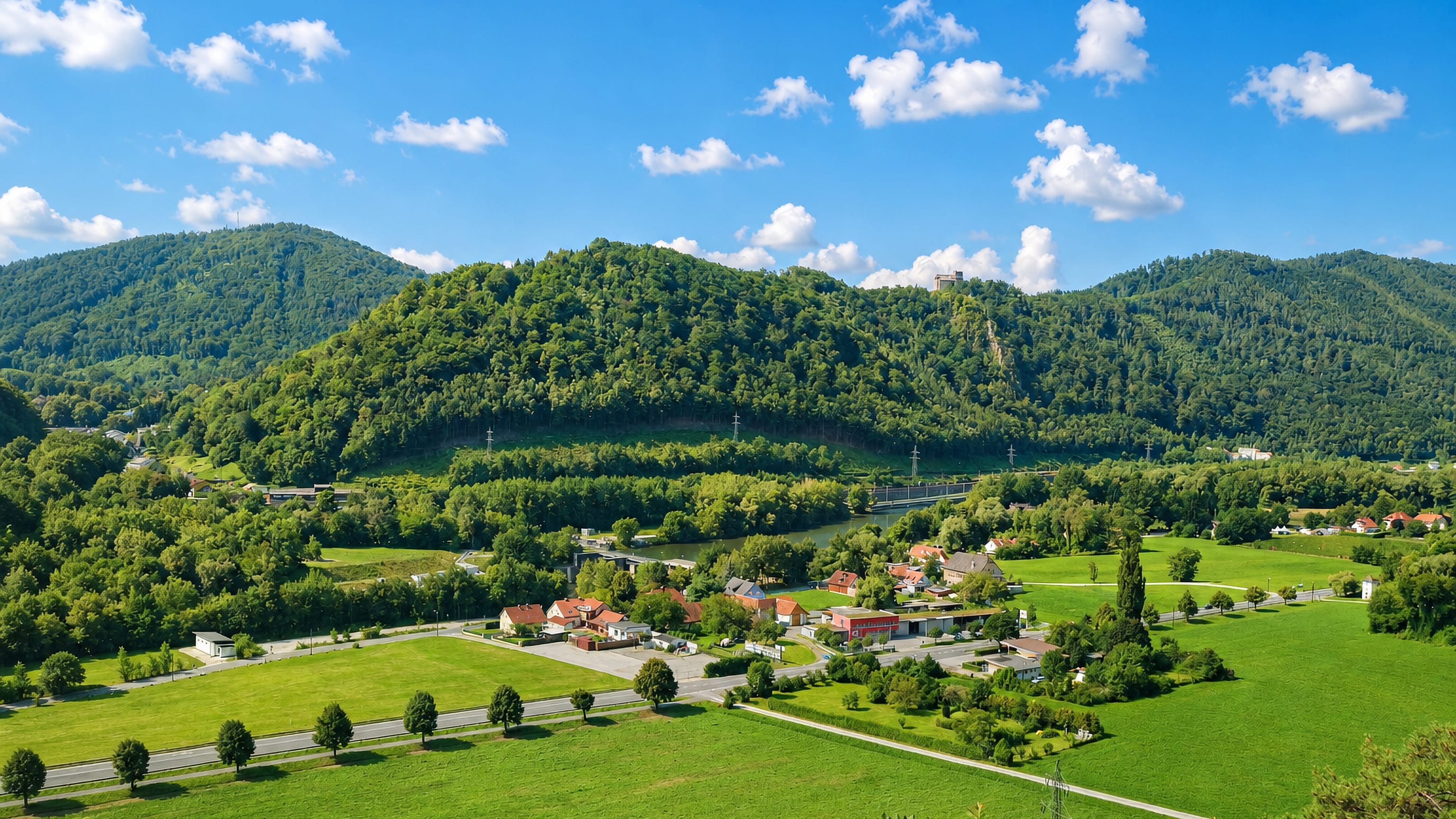 Green Mur valley meadows, riverside houses and wooded hills with a ridge-top ruin at Weinzodl, Graz.