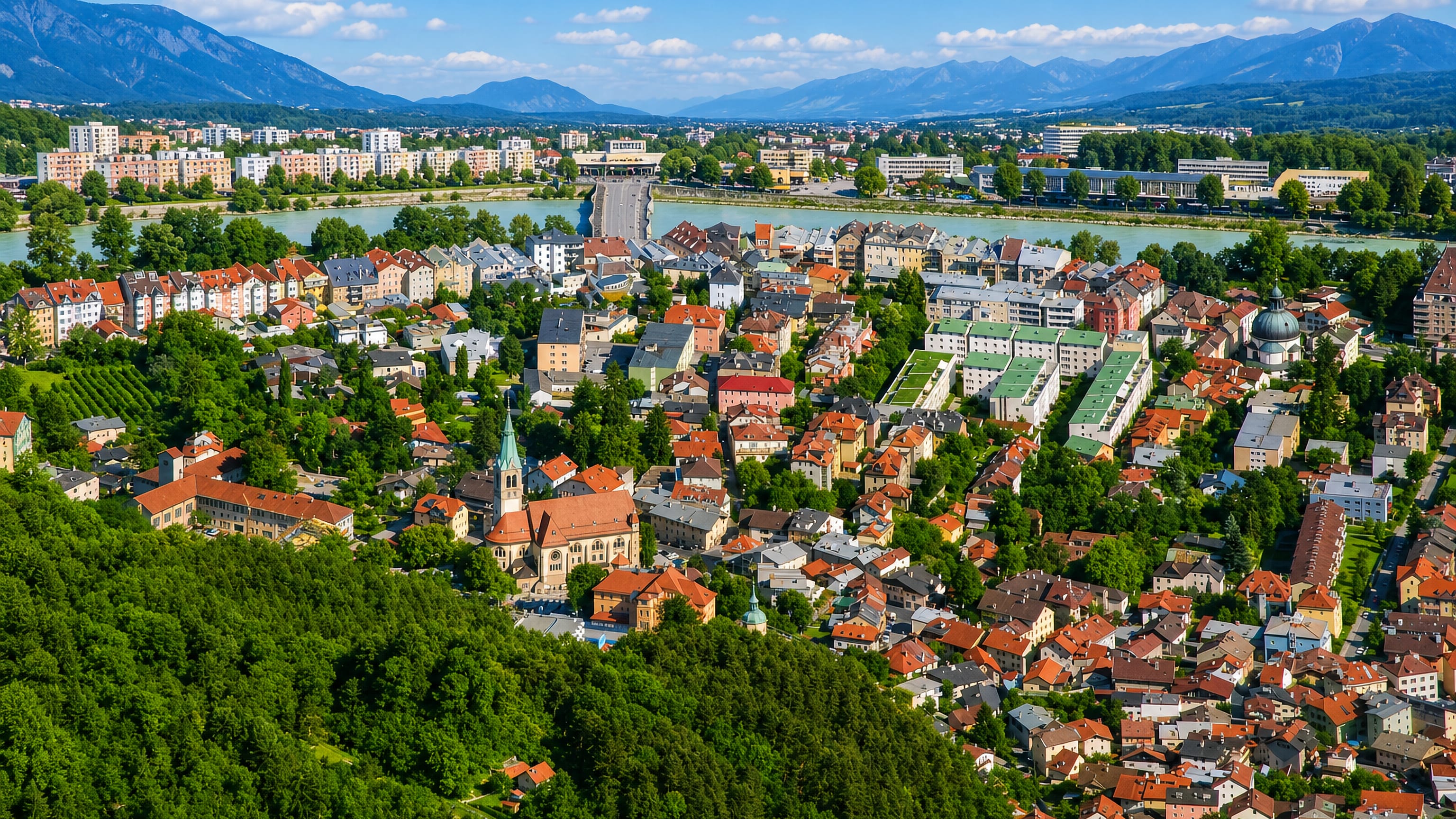 Hillside view over a church tower and rooftops toward the Inn river and Tyrolean mountains at Hötting, Innsbruck