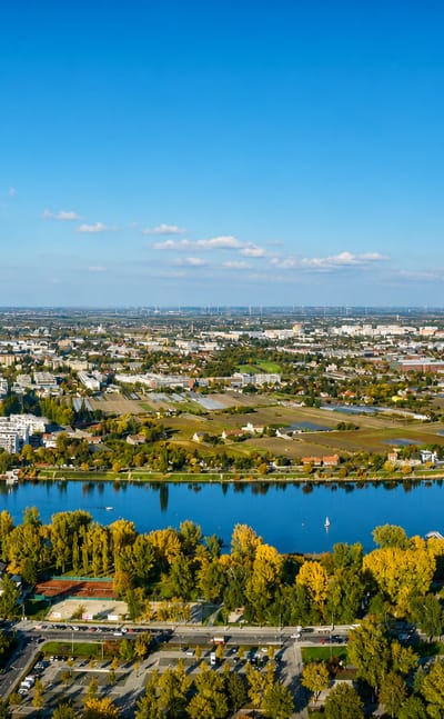 Aerial over the Danube at Floridsdorf, Vienna, with autumn trees, riverside housing and distant wind turbines