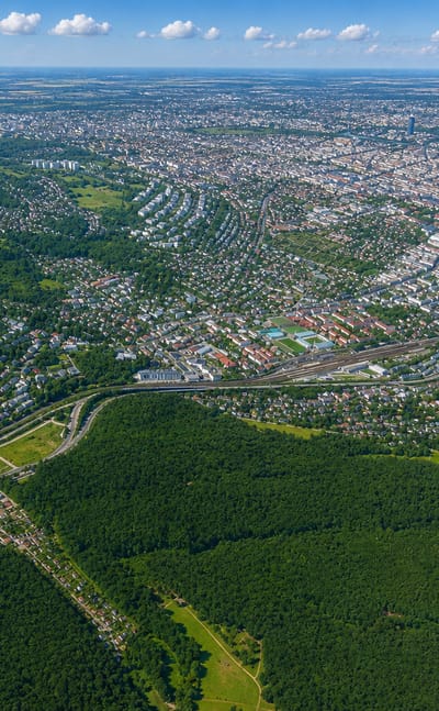 High aerial over western Vienna's Penzing district with the wooded Vienna Woods hills, residential streets and the Danube beyond.