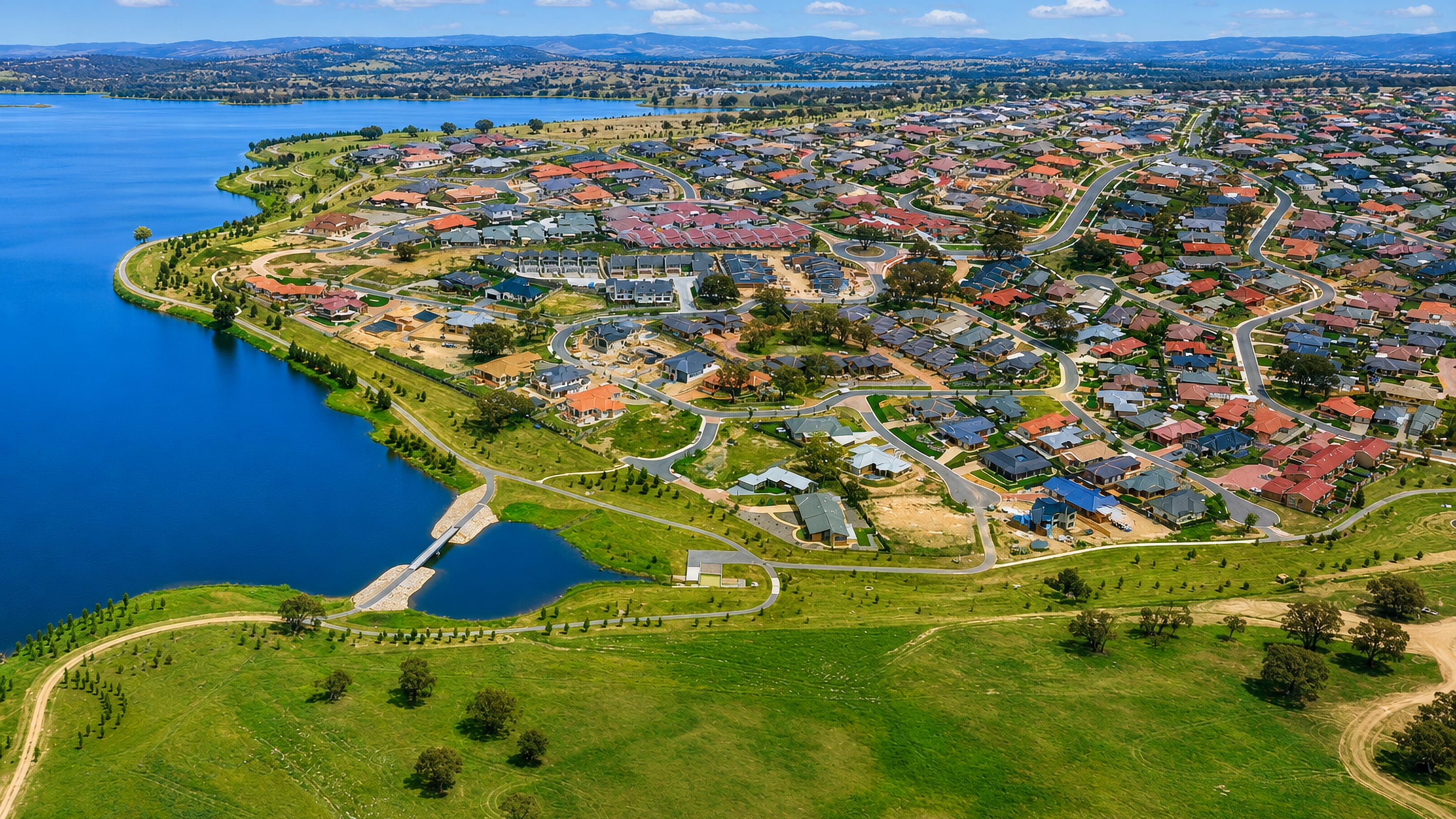 Aerial view of Amaroo's tiled-roof homes beside a Canberra lake, with open grassland in the foreground.