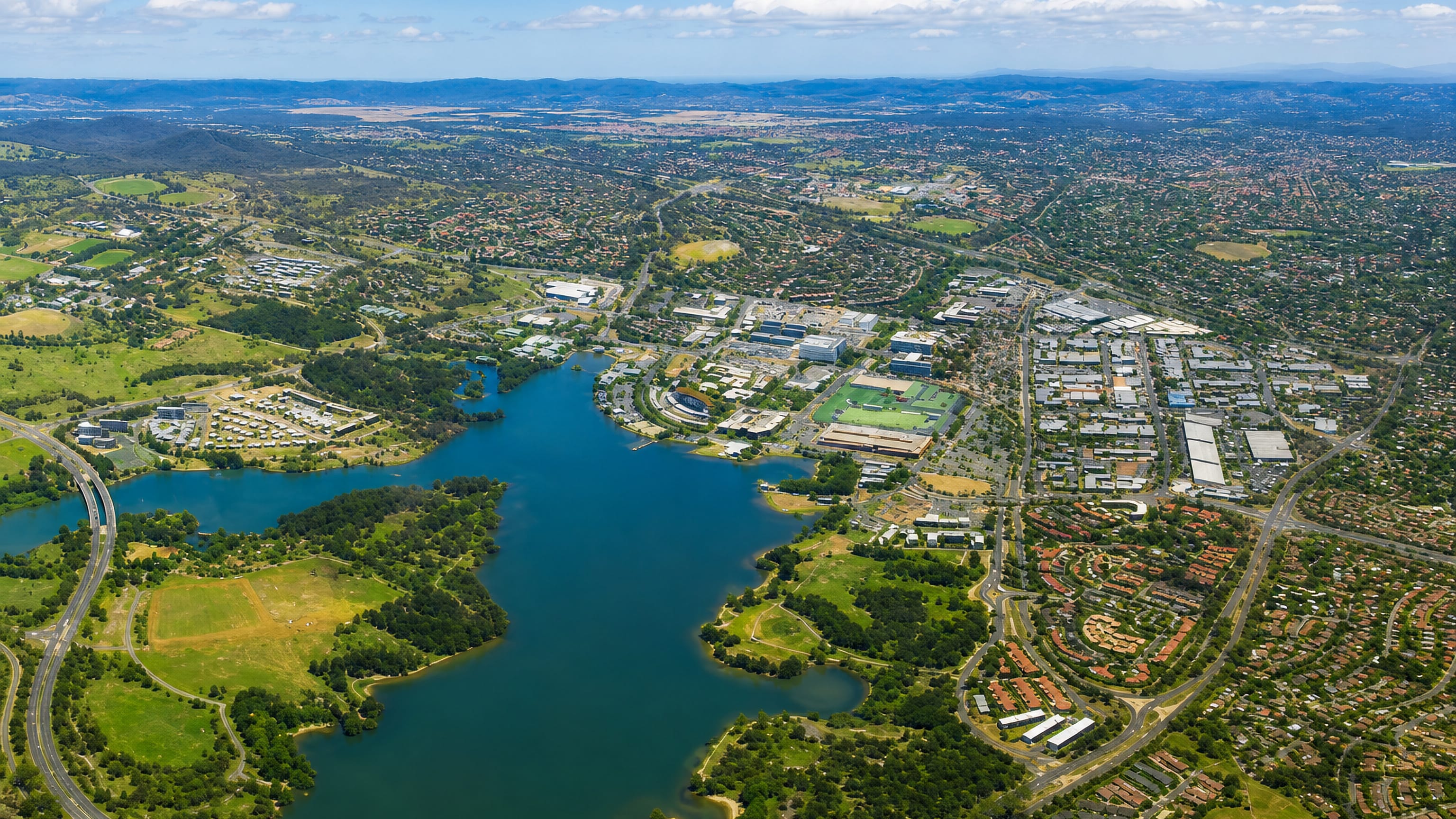 Belconnen, Canberra, from the air: Lake Ginninderra with the town centre, suburbs and distant ranges beyond.
