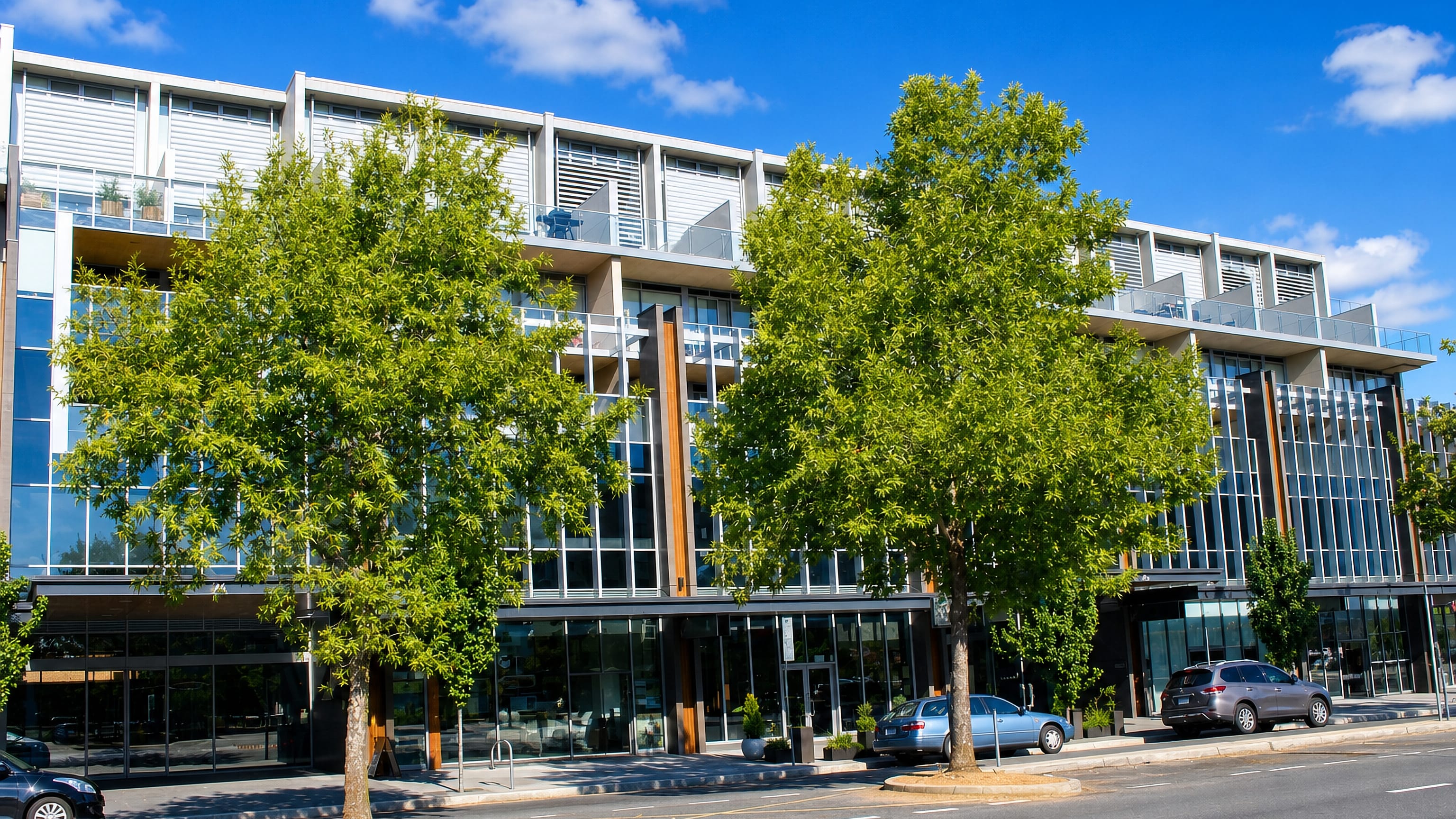 Contemporary mixed-use building with ground-floor shops on a tree-lined street in Braddon, Canberra.