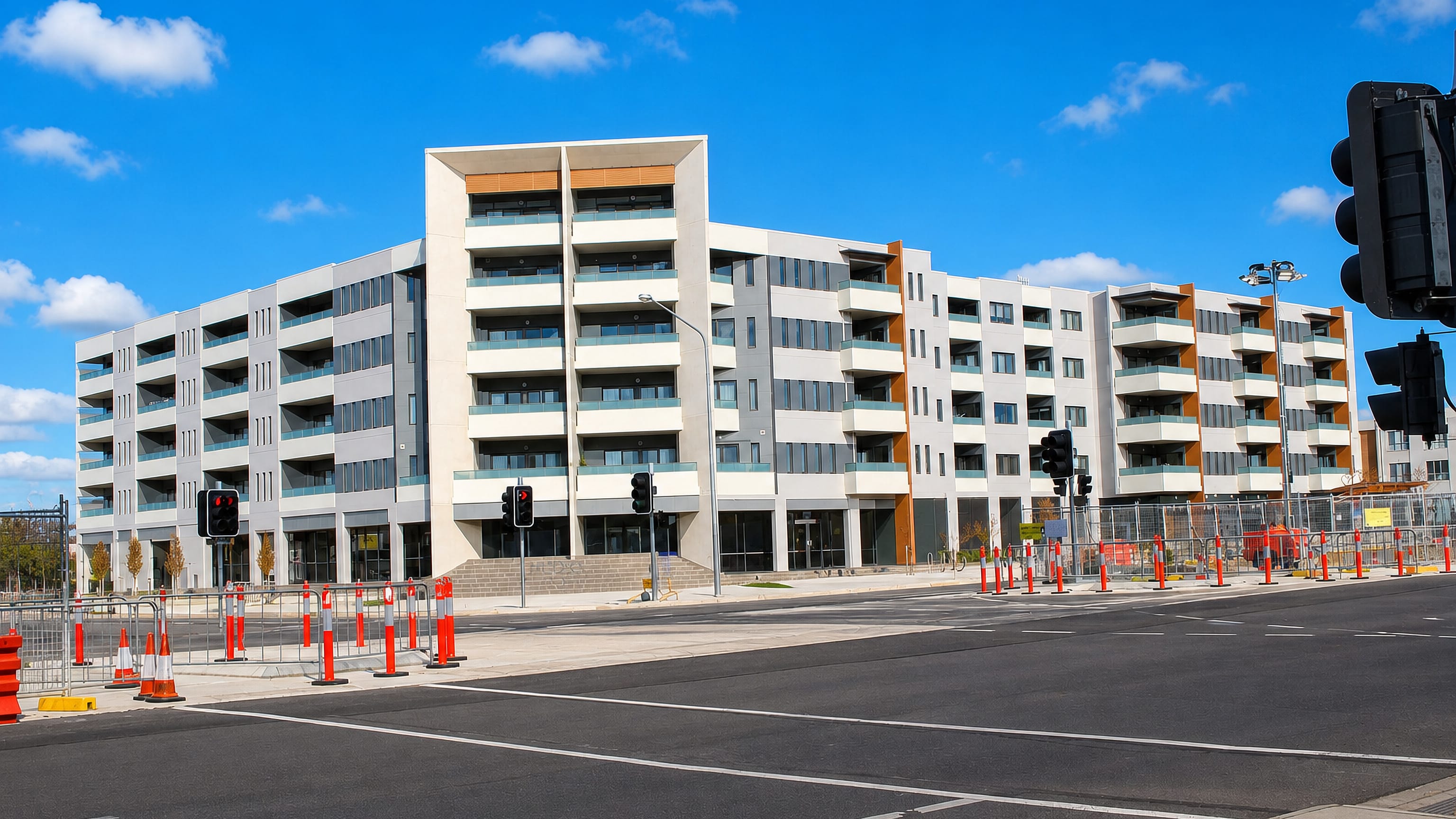 New five-storey apartment block behind roadworks barriers at a wide intersection in Harrison, Canberra.