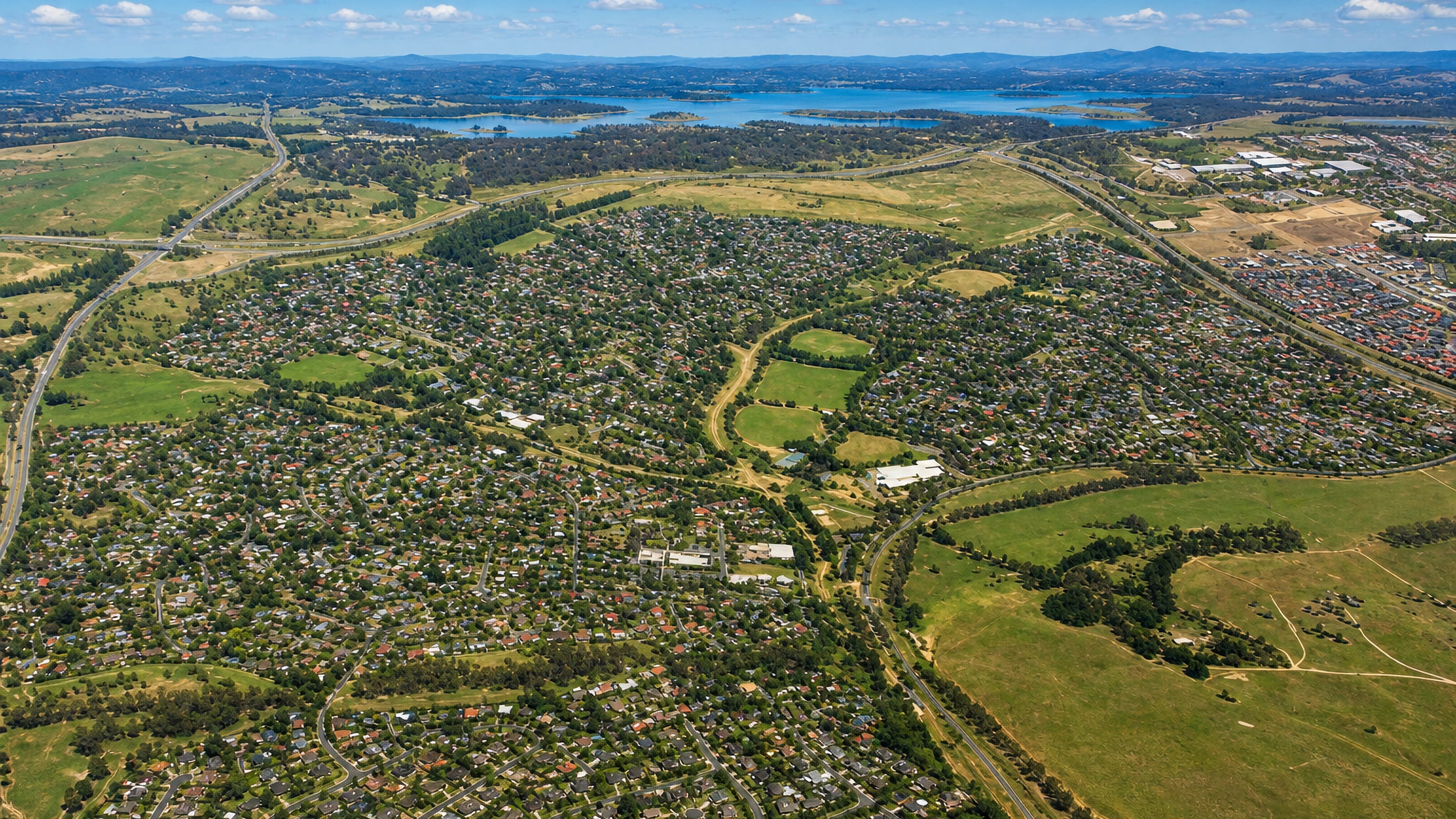 Aerial view over the suburb of Kaleen, Canberra, with a lake and open grassland beyond.