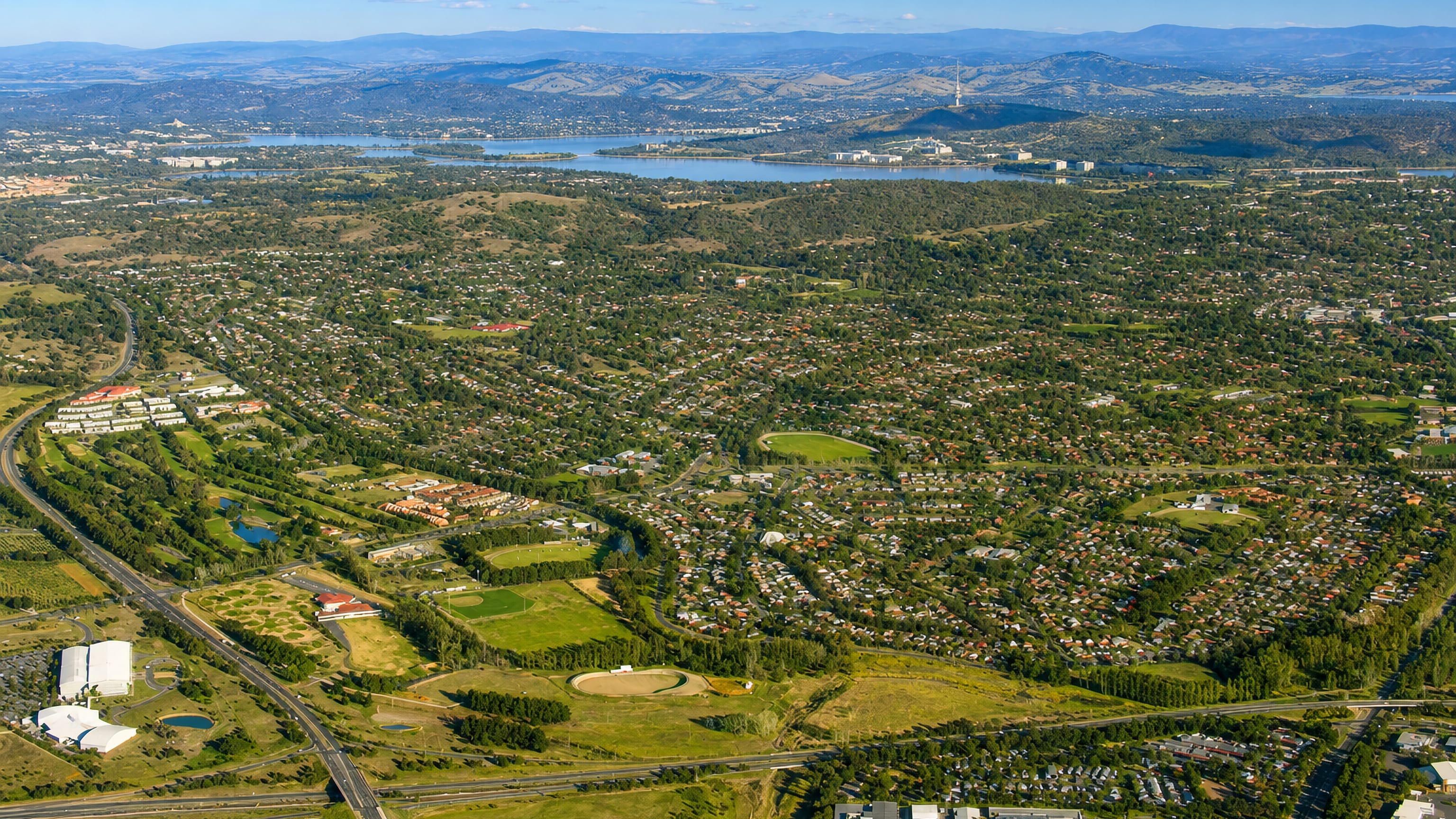 Aerial over the leafy suburb of Narrabundah toward Lake Burley Griffin and Black Mountain Tower, Canberra.