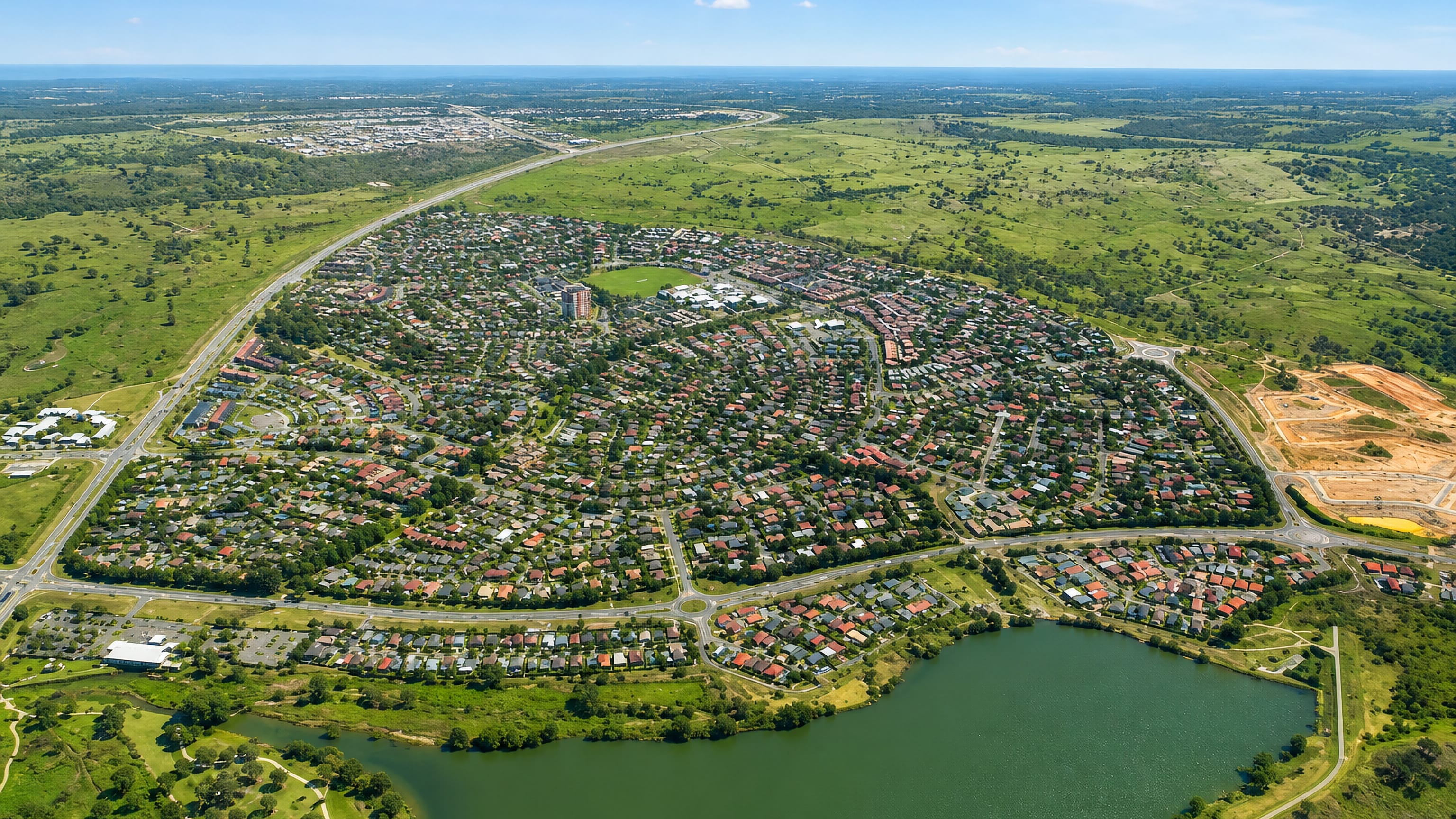 Aerial view of Palmerston, Canberra, showing tiled-roof suburban streets beside a lake and open grassland.