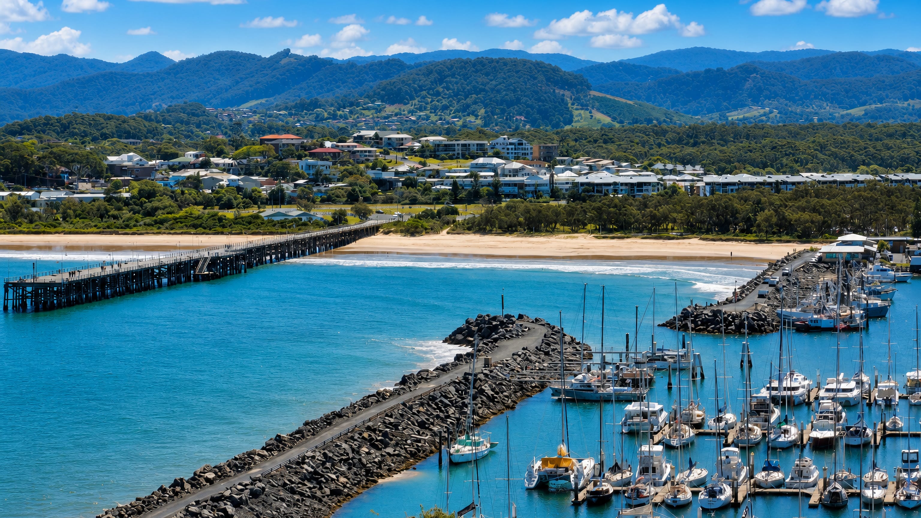 Coffs Harbour marina, rock breakwater and historic timber jetty below the forested ranges of the NSW coast.