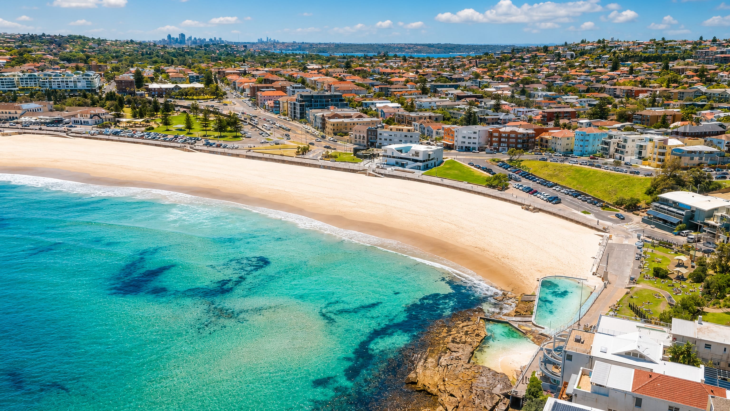 Bondi Beach curving between turquoise surf and the suburb, with the Icebergs ocean pool and Sydney skyline