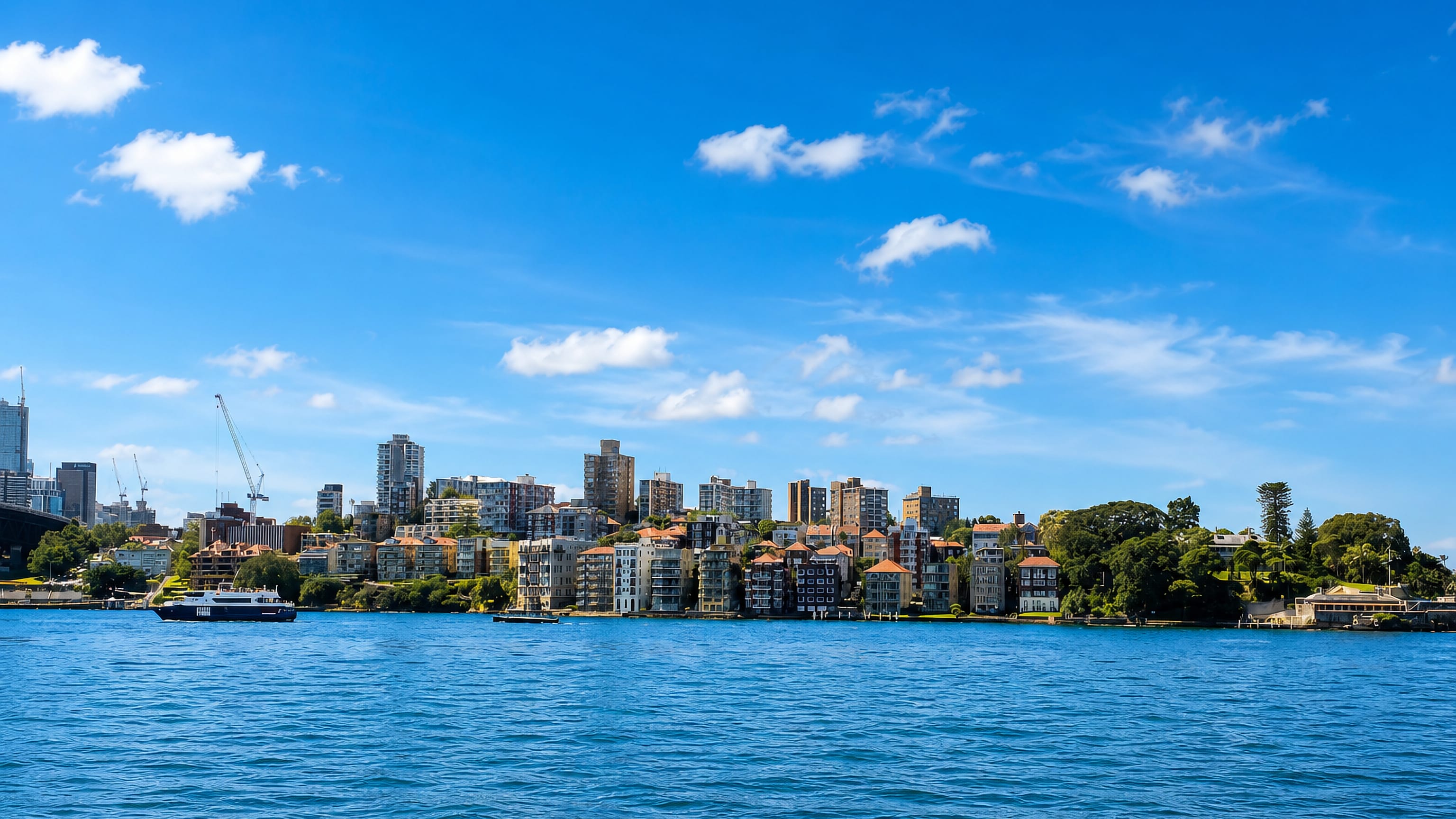 Kirribilli's harbourside apartments and greenery seen across Sydney Harbour, bridge edge at left.