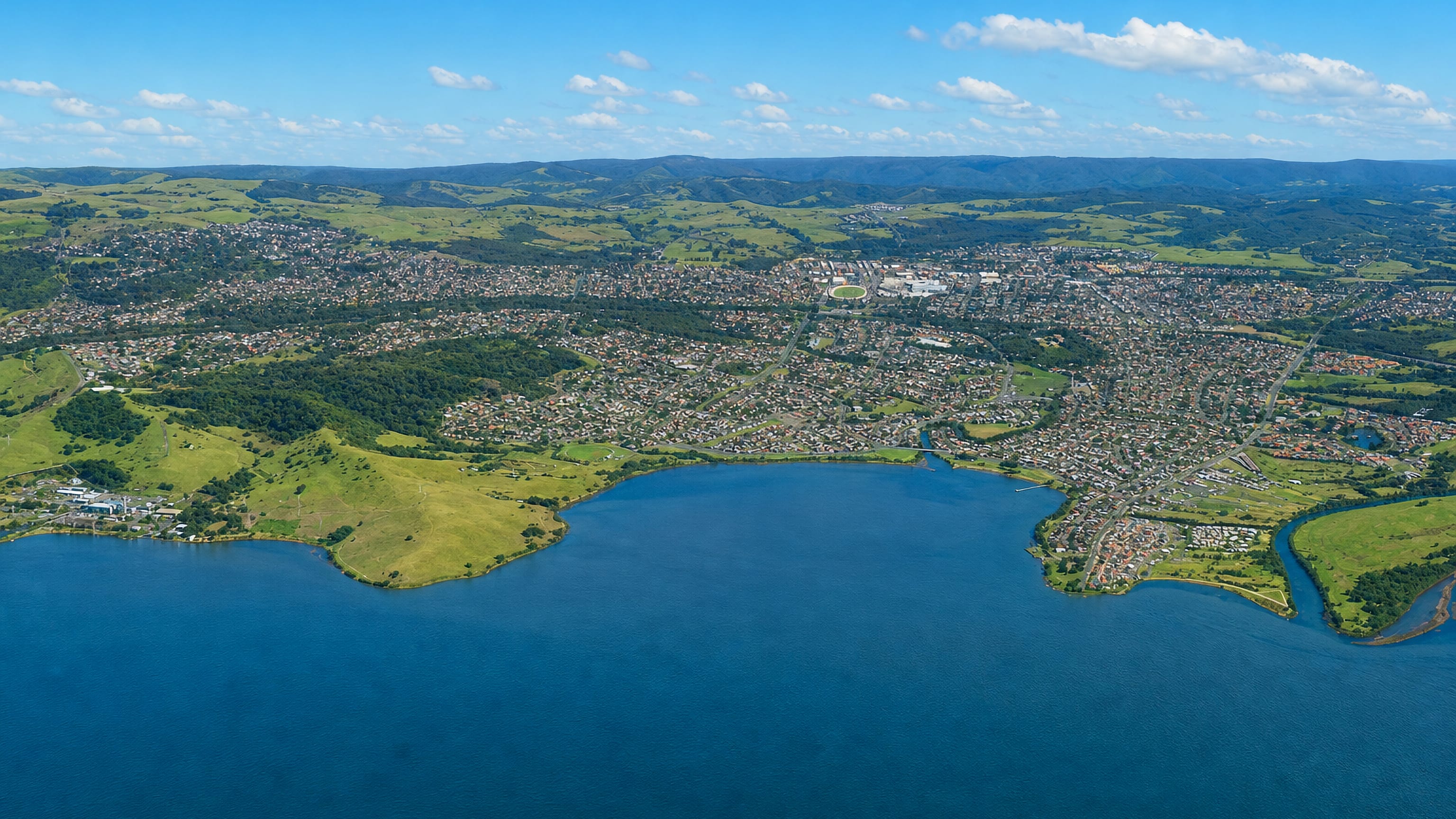 Aerial view of Dapto spreading between Lake Illawarra and the green escarpment hills, New South Wales.