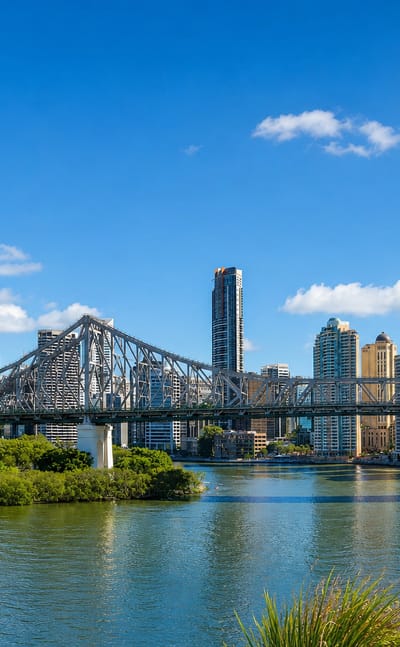 Brisbane's Story Bridge and CBD skyline rising above the Brisbane River, framed by riverside greenery.