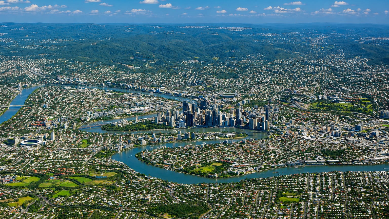 Aerial view over East Brisbane suburbs and the winding Brisbane River toward the city centre.