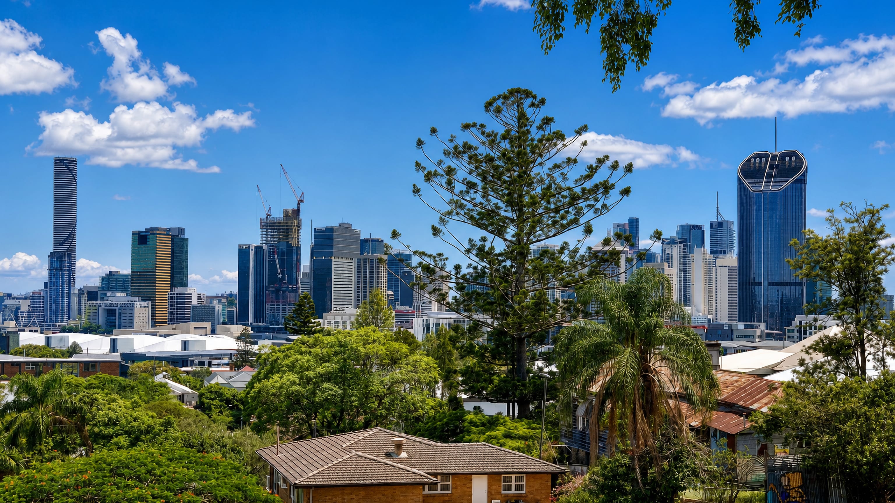 Brisbane's skyline seen across the leafy rooftops of Highgate Hill, with a brick cottage in the foreground.