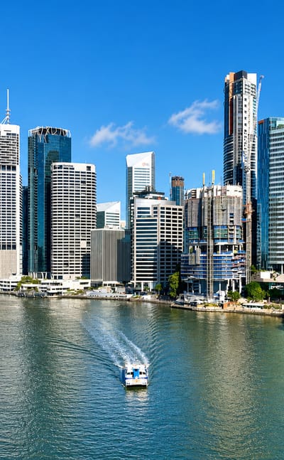 Brisbane CBD skyline of glass towers across the Brisbane River, seen from Kangaroo Point with a CityCat ferry passing