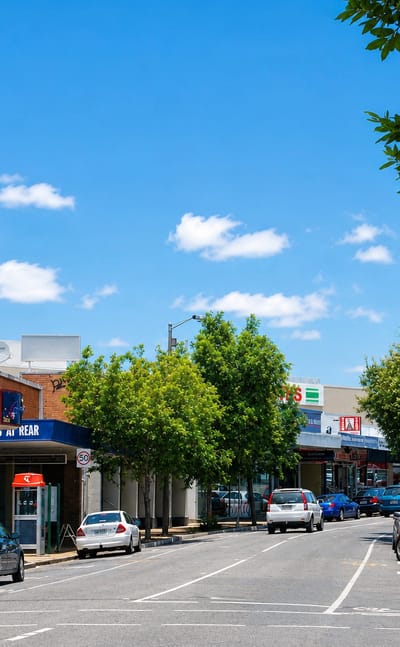 Tree-lined shopping street with shopfronts and parked cars in the Brisbane suburb of Nundah.