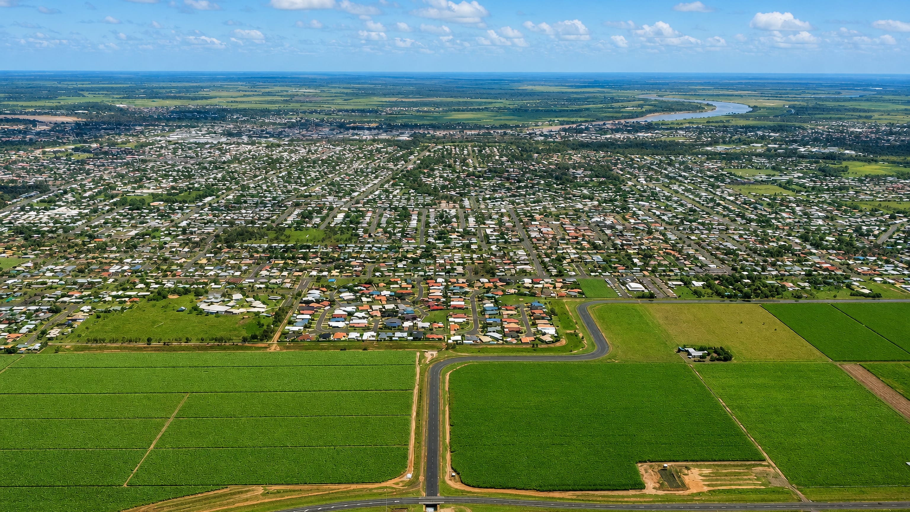 Bundaberg's suburbs ringed by sugarcane fields with the Burnett River winding beyond, seen from the air.