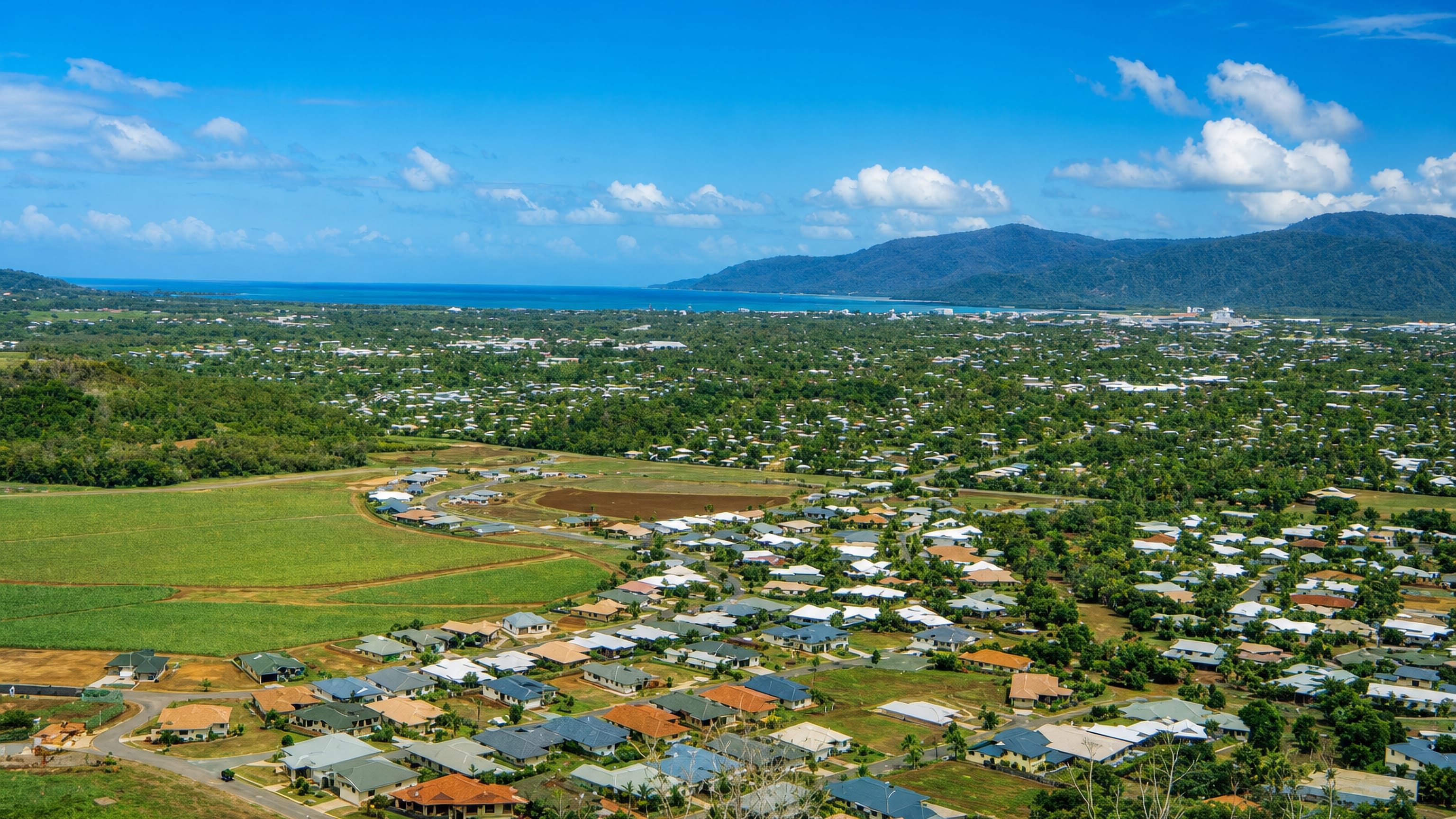 Edmonton's suburban houses and sugarcane fields south of Cairns, framed by rainforest ranges and the Coral Sea.