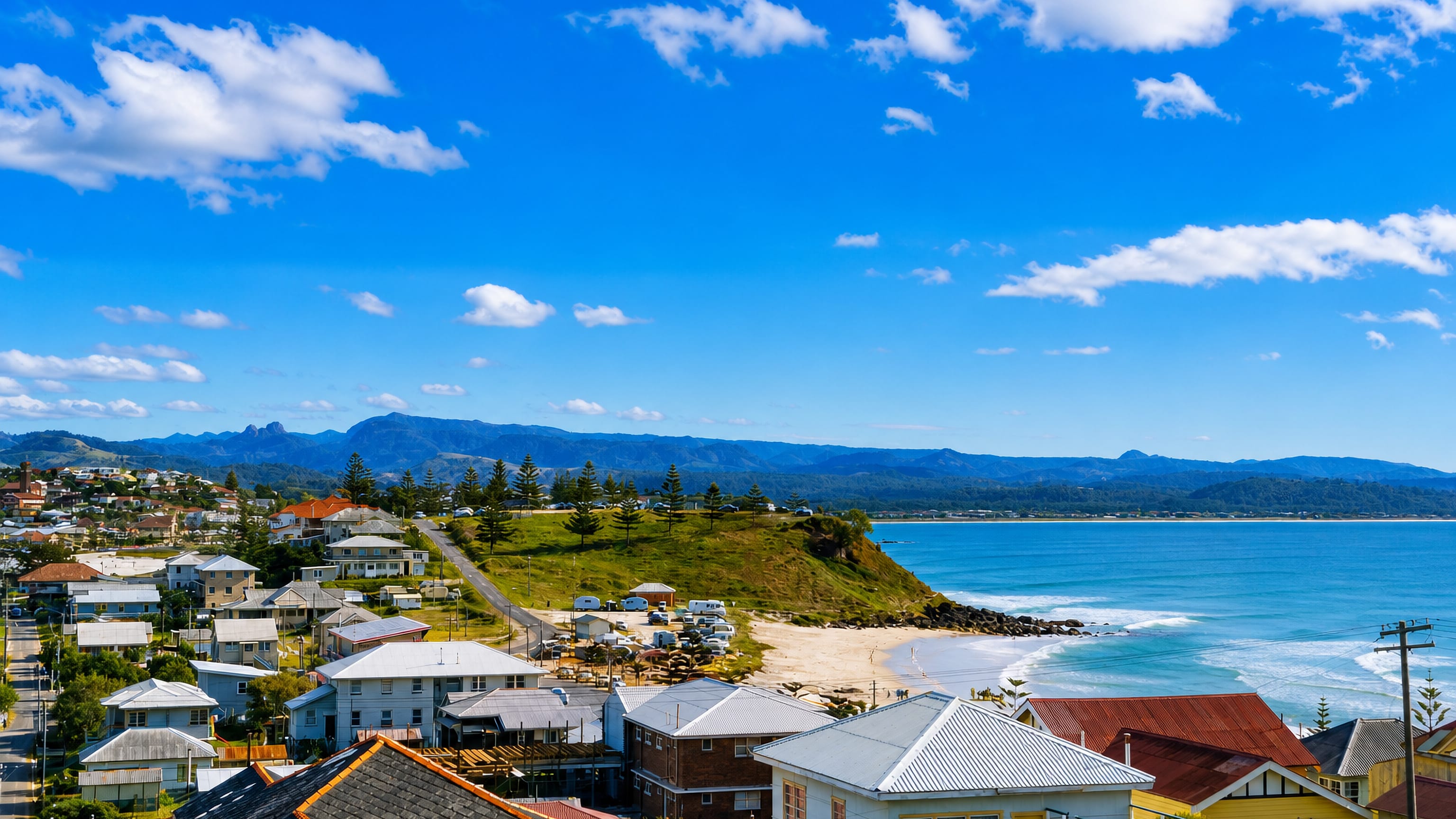 Low-rise coastal houses above a curving surf beach and grassy headland at Coolangatta on the Gold Coast