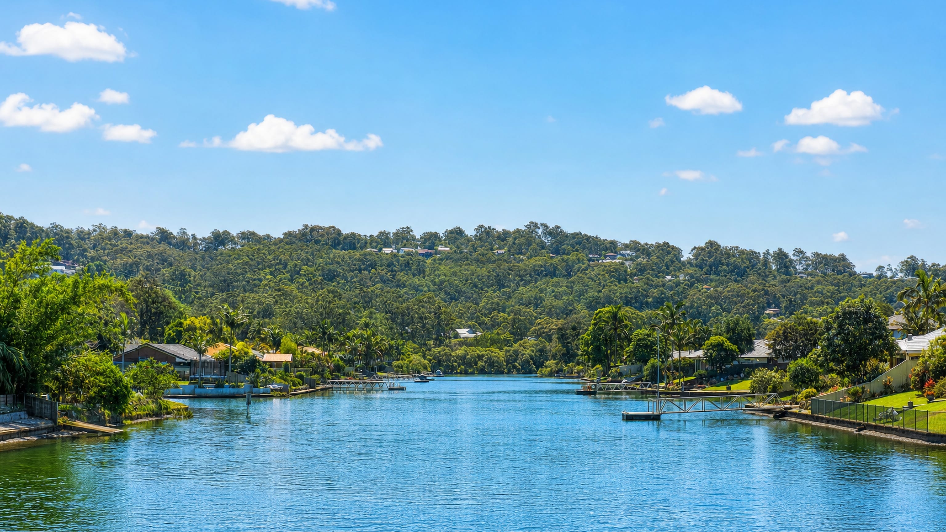 Canal lined with waterfront homes and jetties below forested hills at Currumbin Waters, Gold Coast.