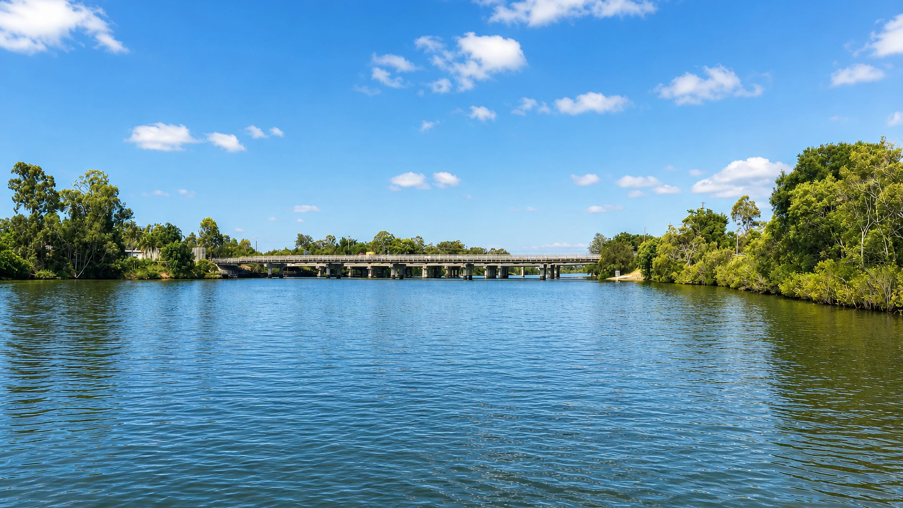 Wide blue river with a low road bridge and bushland banks at Oxenford on the Gold Coast.