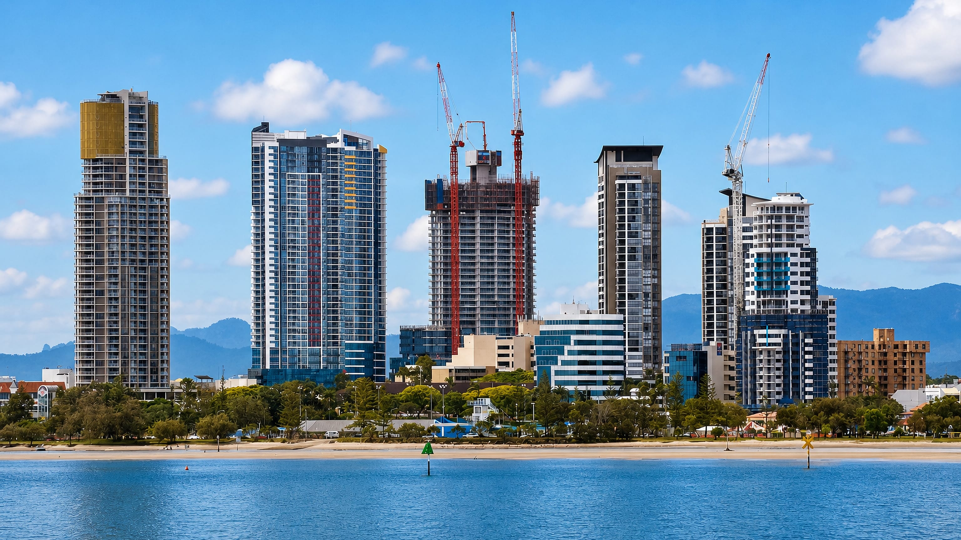 Southport's high-rise skyline on the Gold Coast Broadwater, with a sandy spit and hinterland ranges behind.