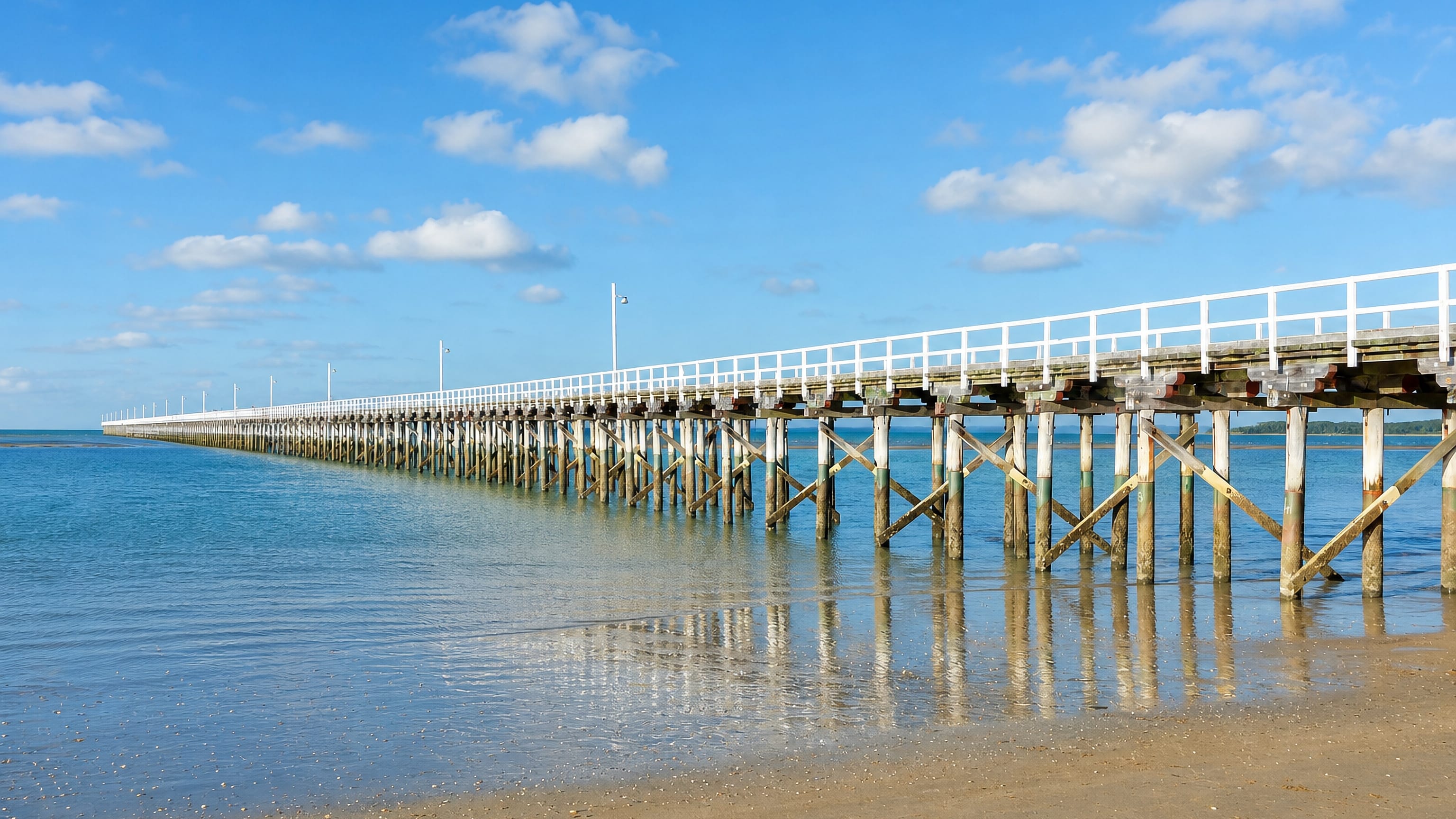 The long timber Urangan Pier reaching out into Hervey Bay from the sandy Urangan foreshore, Queensland.